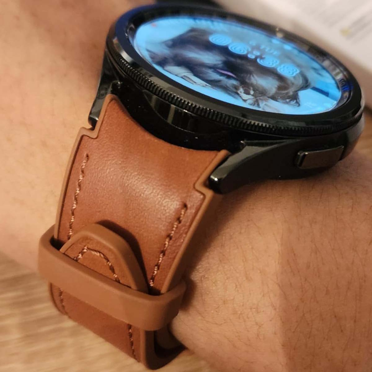 Una correa de reloj de cuero marrón está en una muñeca. La esfera del reloj muestra un perro. El reloj es negro con un bisel negro.
