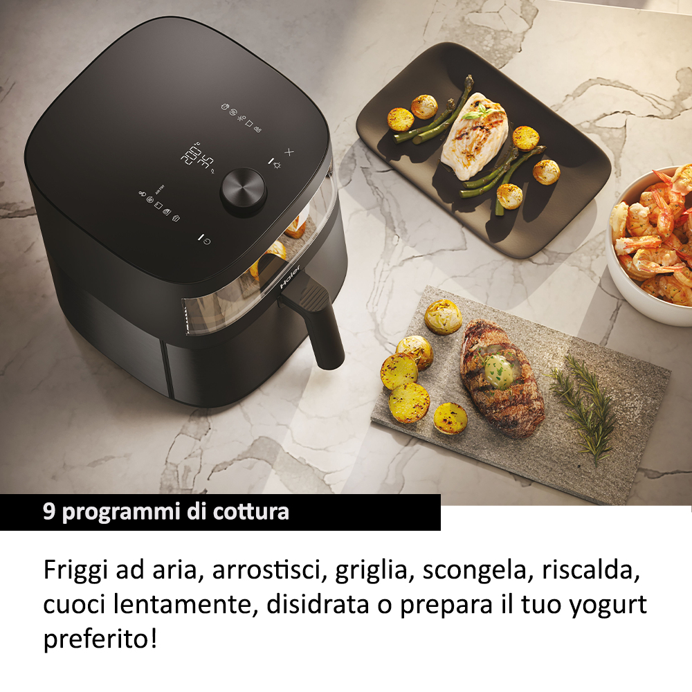 Una friggitrice ad aria nera con cibo sui piatti. Una bistecca con burro, gamberi, pesce, patate e asparagi sono visibili.