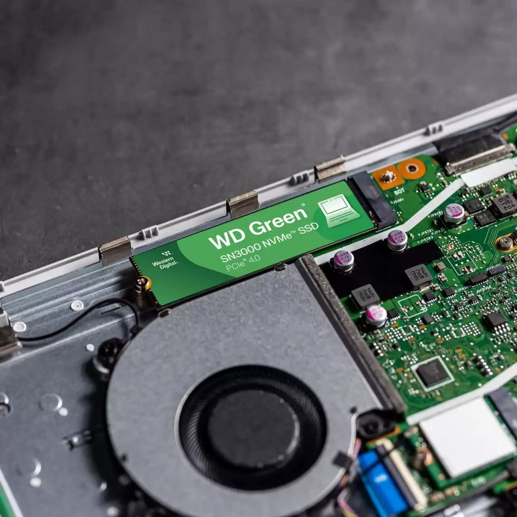 Wnętrze laptopa z zainstalowanym dyskiem WD Green SN3000 NVMe SSD. Zielona karta SSD jest umieszczona na płycie obwodu w pobliżu wentylatora.