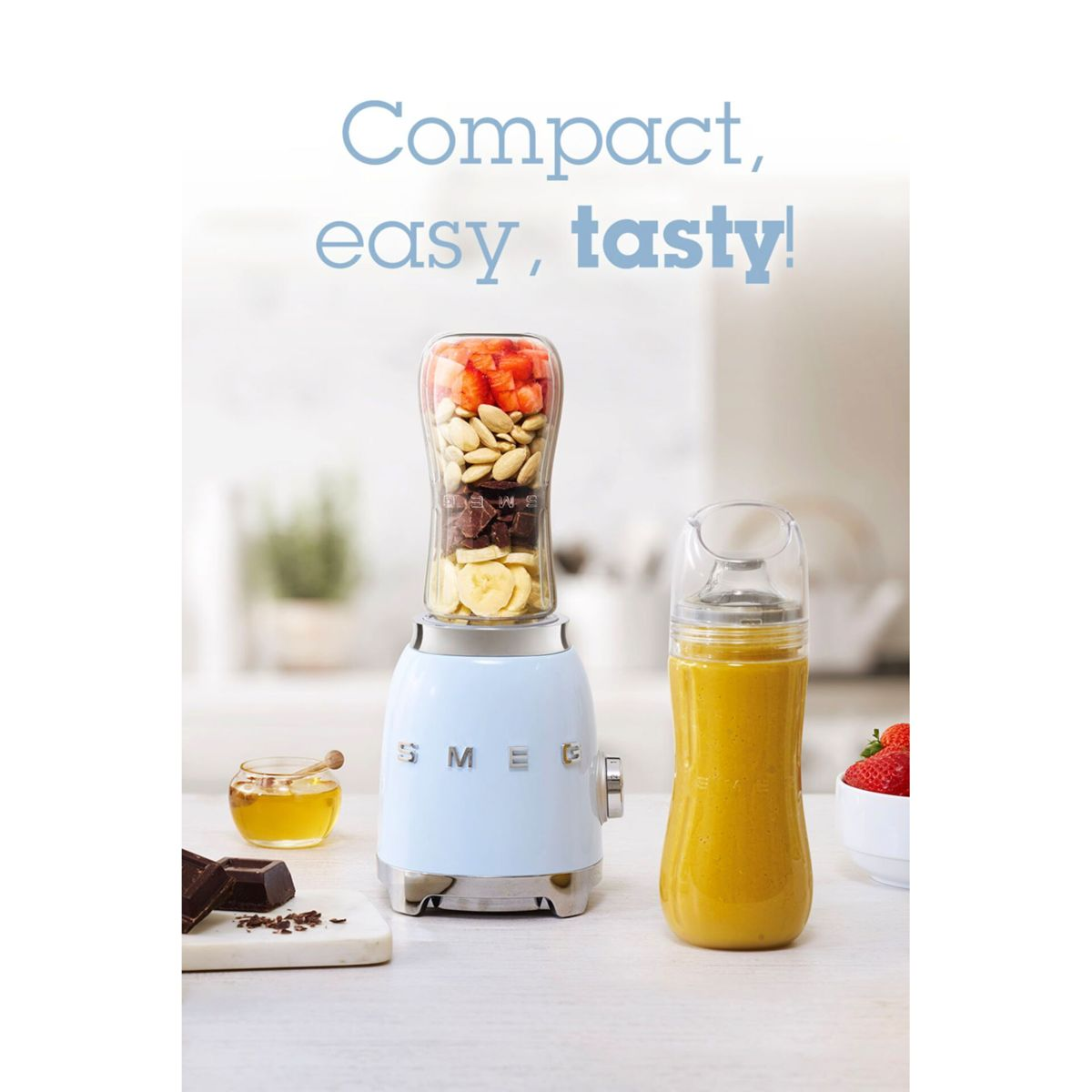Jasnoniebieski blender ze składnikami, obok butelki smoothie. Inne przedmioty to miód, czekolada i truskawki.