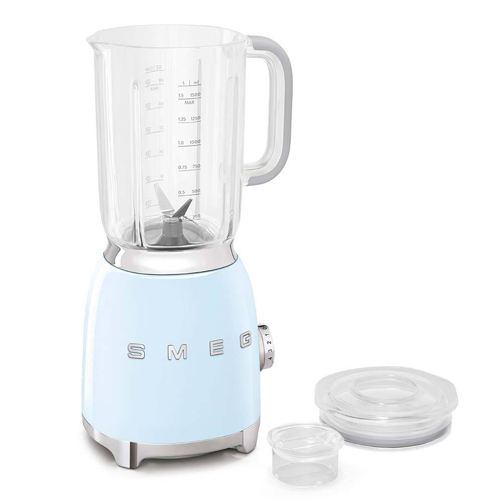 Una batidora SMEG azul claro con un frasco de vidrio transparente. El frasco tiene medidas. Una tapa y una taza pequeña están al lado de la batidora.