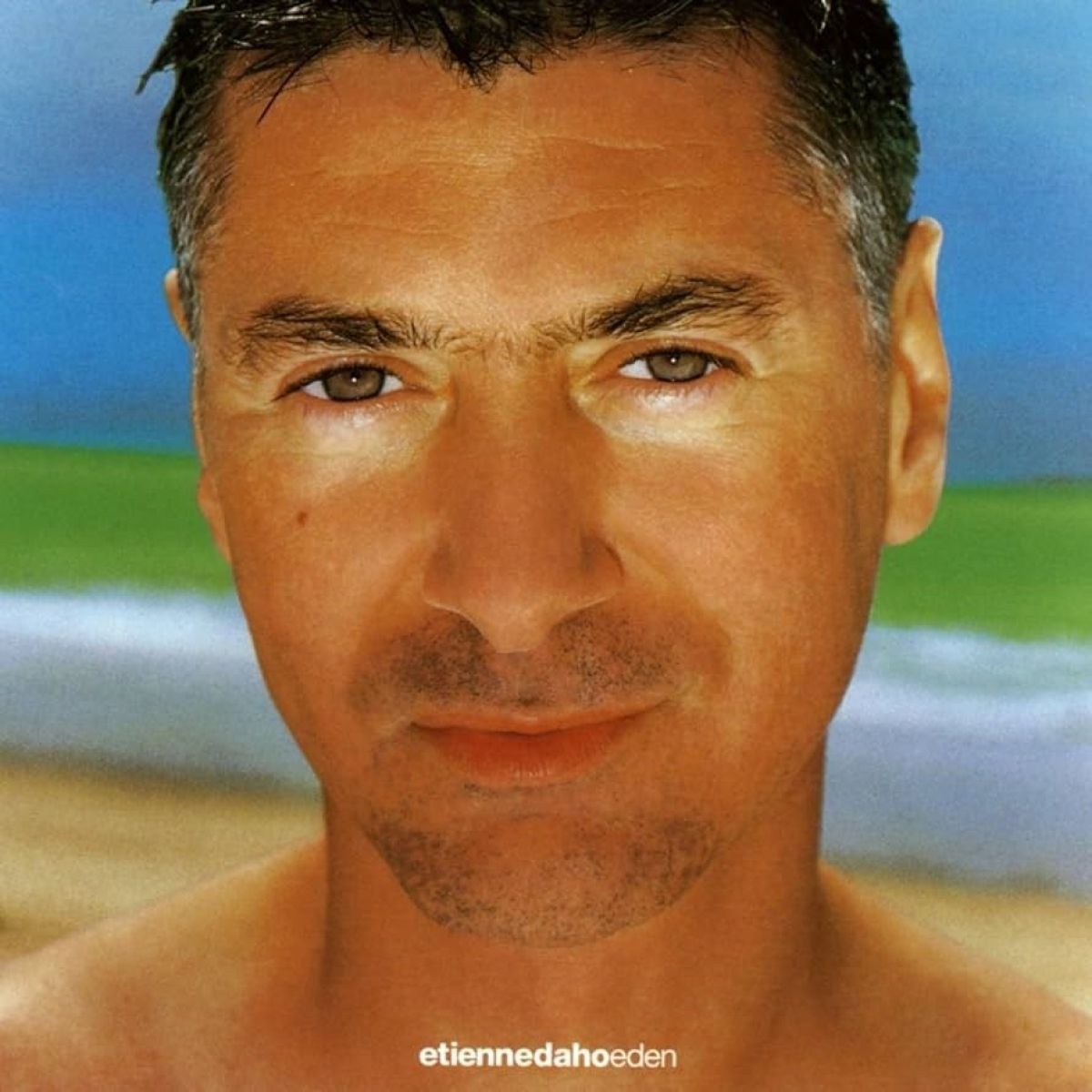 Un uomo con capelli corti e grigi e carnagione abbronzata guarda direttamente lo spettatore. Lo sfondo mostra una spiaggia e il cielo.