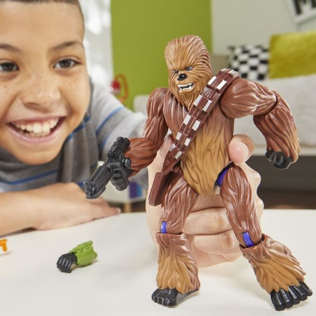 Ein lächelnder Junge hält eine Chewbacca-Actionfigur mit einem Blaster. Ein abgetrennter grüner Arm liegt auf der weißen Oberfläche.