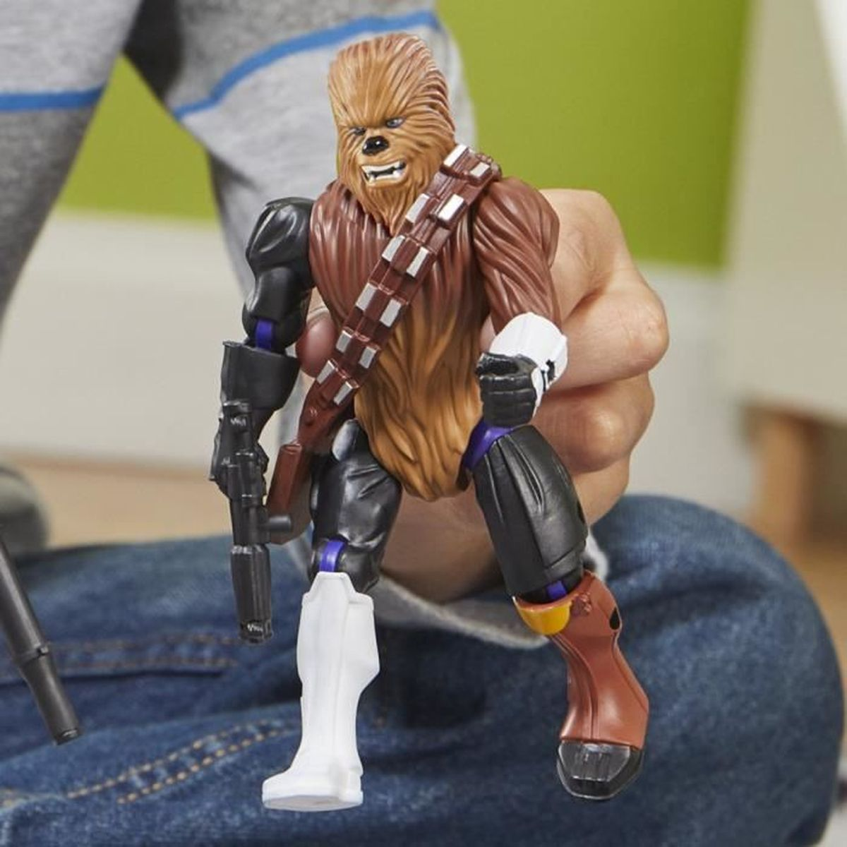 Eine Chewbacca-Actionfigur in der Hand einer Person. Die Figur ist braun, schwarz und weiß, mit einem Blaster. Der Hintergrund ist eine grüne Wand.