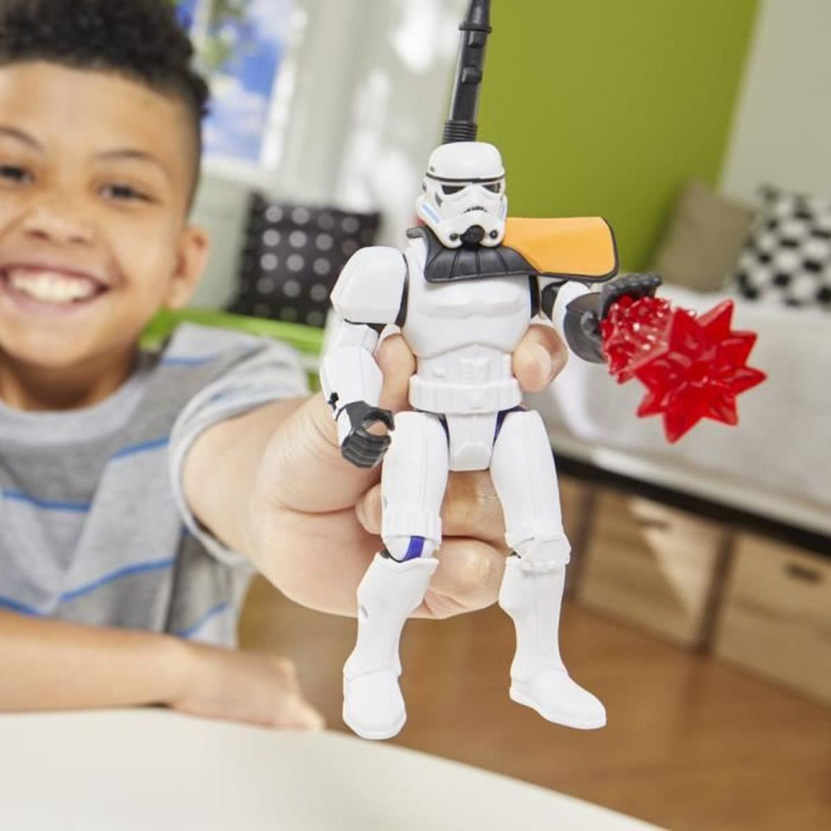 Un niño sonriente sostiene una figura de acción de Stormtrooper. La figura es blanca con un arma negra y una estrella roja.