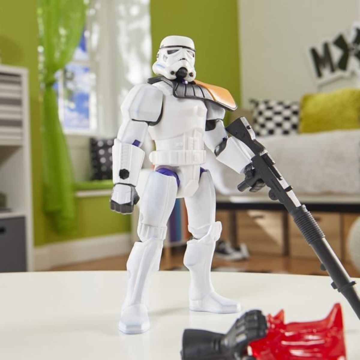 Una figura de acción de Stormtrooper está sobre una superficie blanca. Tiene un arma negra. El fondo tiene una ventana y un sofá con almohadas.