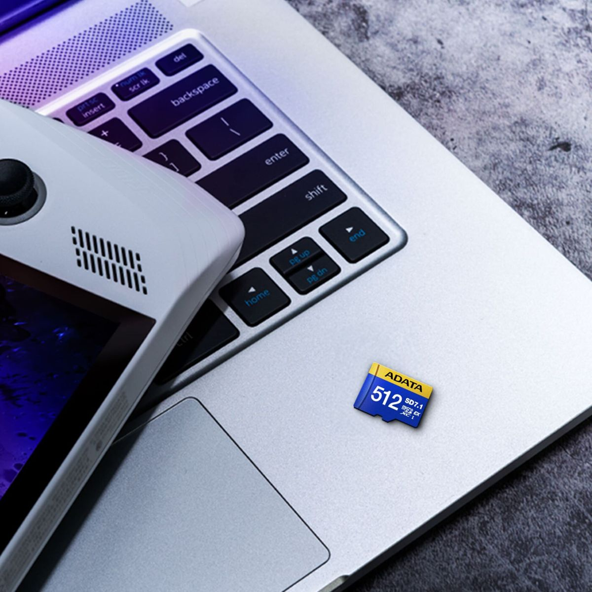 Ein Laptop mit Tastatur und einem Spielgerät. Eine blau-gelbe SD-Karte liegt auf dem Laptop. Der Hintergrund ist grau.