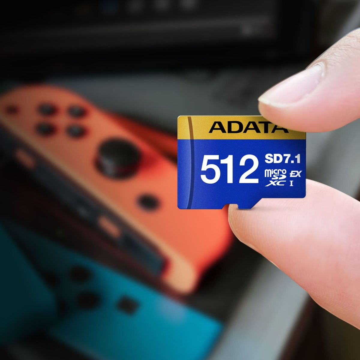 Eine Hand hält eine blaue und goldene 512GB ADATA SD-Karte. Dahinter ist ein verschwommener orangefarbener und blauer Gamecontroller.