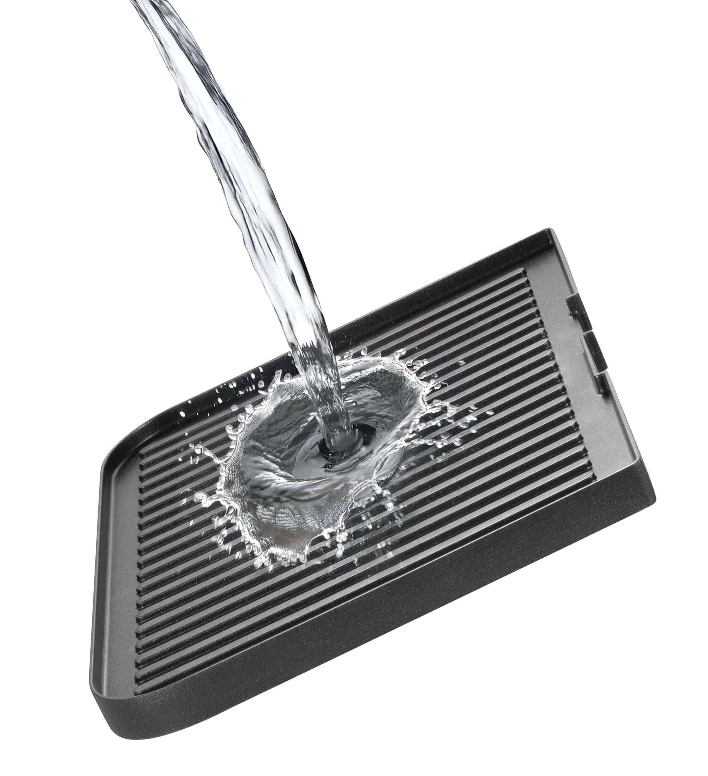 Wasser gießt auf eine schwarze, gerippte Grillpfanne. Wasser spritzt beim Aufprall. Weißer Hintergrund.