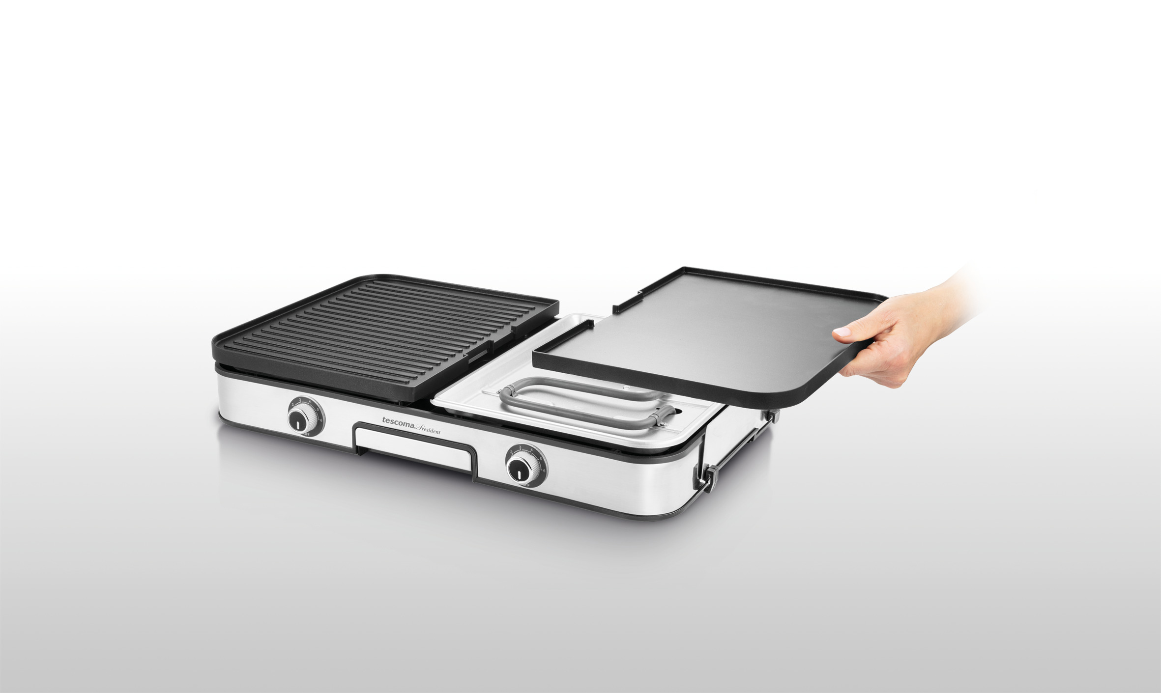 Ein weißer und silberner Elektrogrill. Eine Hand entfernt eine flache schwarze Platte. Der Grill hat eine Grillplatte und eine geriffelte Platte.