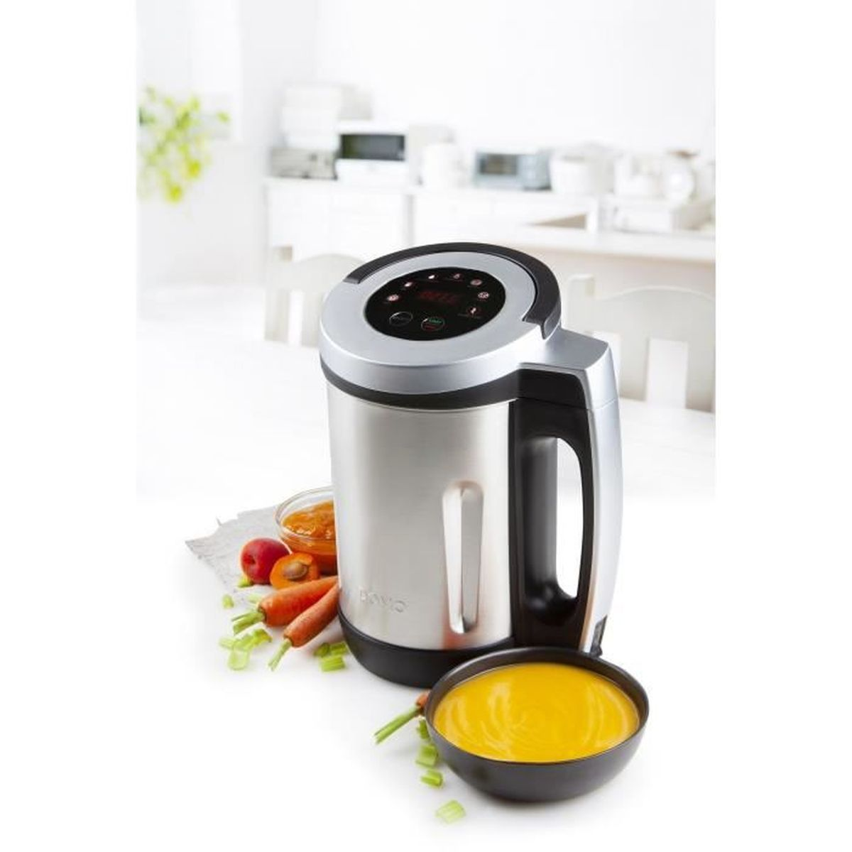 Un'apparecchio per fare la zuppa argentato con maniglia e controlli neri. Davanti ci sono ciotole di zuppa, carote e frutta. Lo sfondo è una cucina bianca.