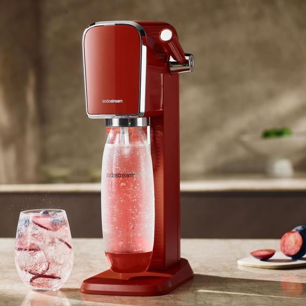 Czerwone urządzenie SodaStream ze szklanką wody gazowanej z owocami. Śliwka jest krojona na stole.