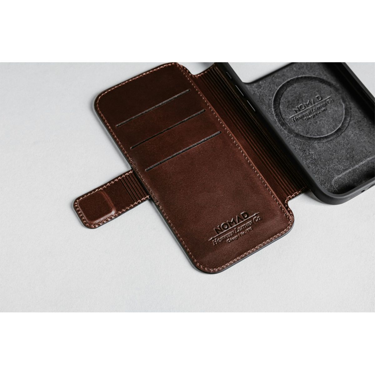 Una custodia per telefono in pelle marrone, aperta, accanto a una custodia per telefono nera. Entrambe le custodie hanno il logo Nomad.