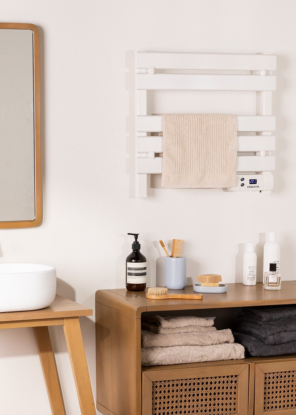 Escena de baño con calentador blanco, toalla, espejo, lavabo, mueble de madera con toallas, artículos de aseo y accesorios.