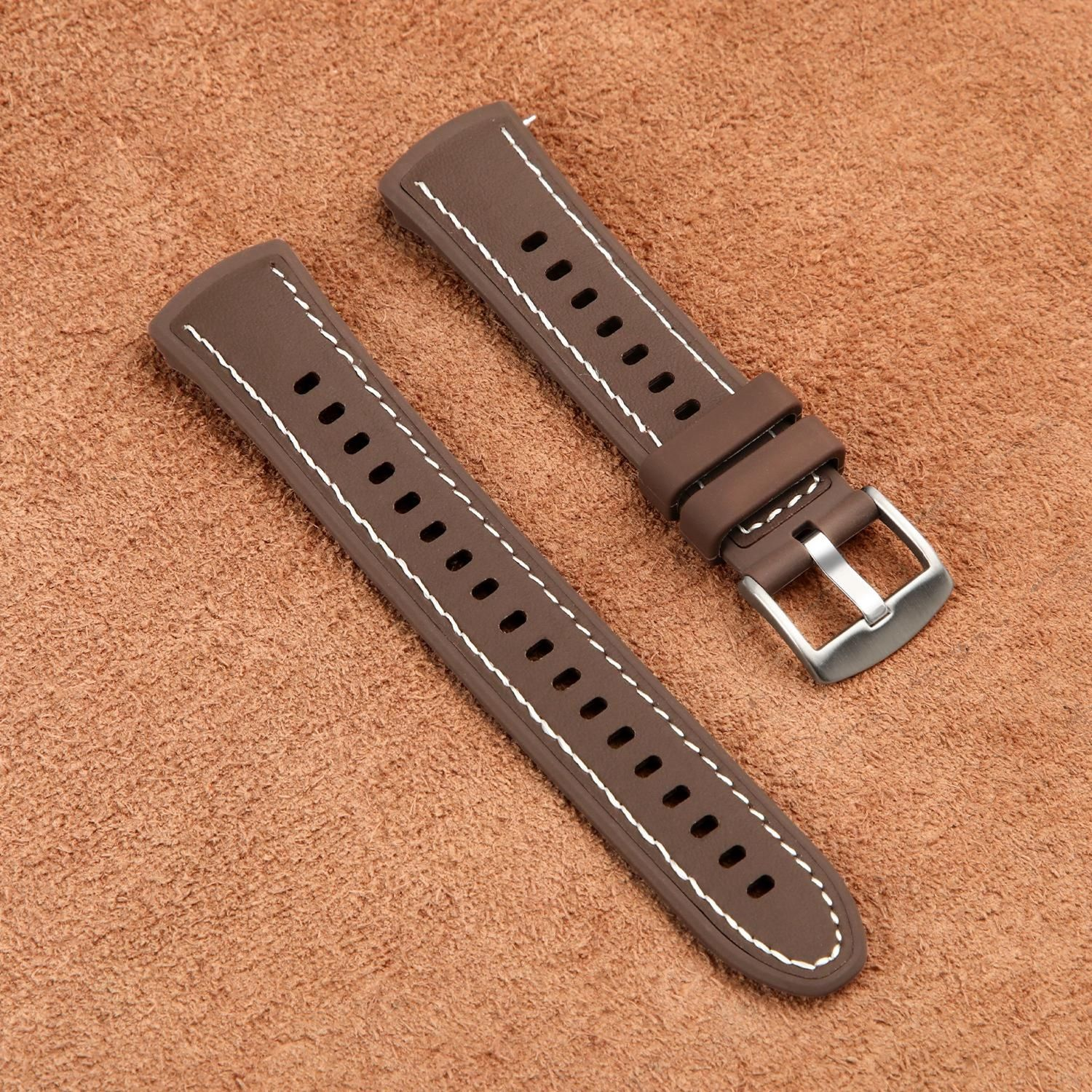 Zwei braune Uhrenarmbänder mit weißen Nähten auf einer strukturierten braunen Oberfläche, Metallschnalle sichtbar.