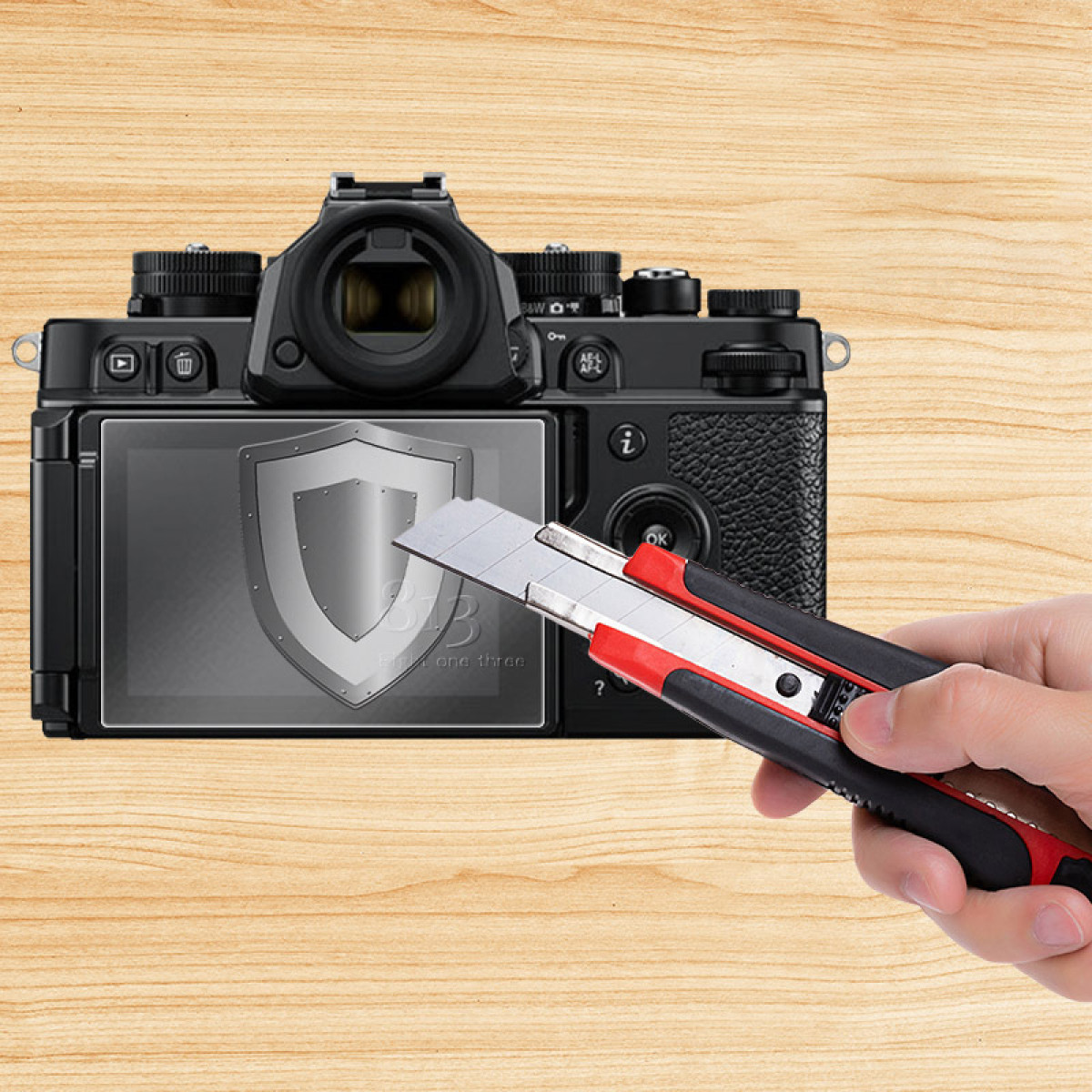 Czarny aparat z ochraniaczem ekranu, nóż przecinający ochraniacz. Drewniane tło. Ręka trzymająca nóż.