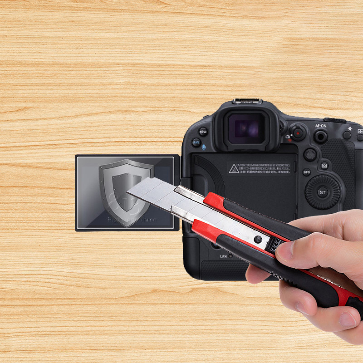 Ręka trzymająca nóż introligatorski nad ekranem aparatu z grafiką tarczy. Tło to drewniana powierzchnia.