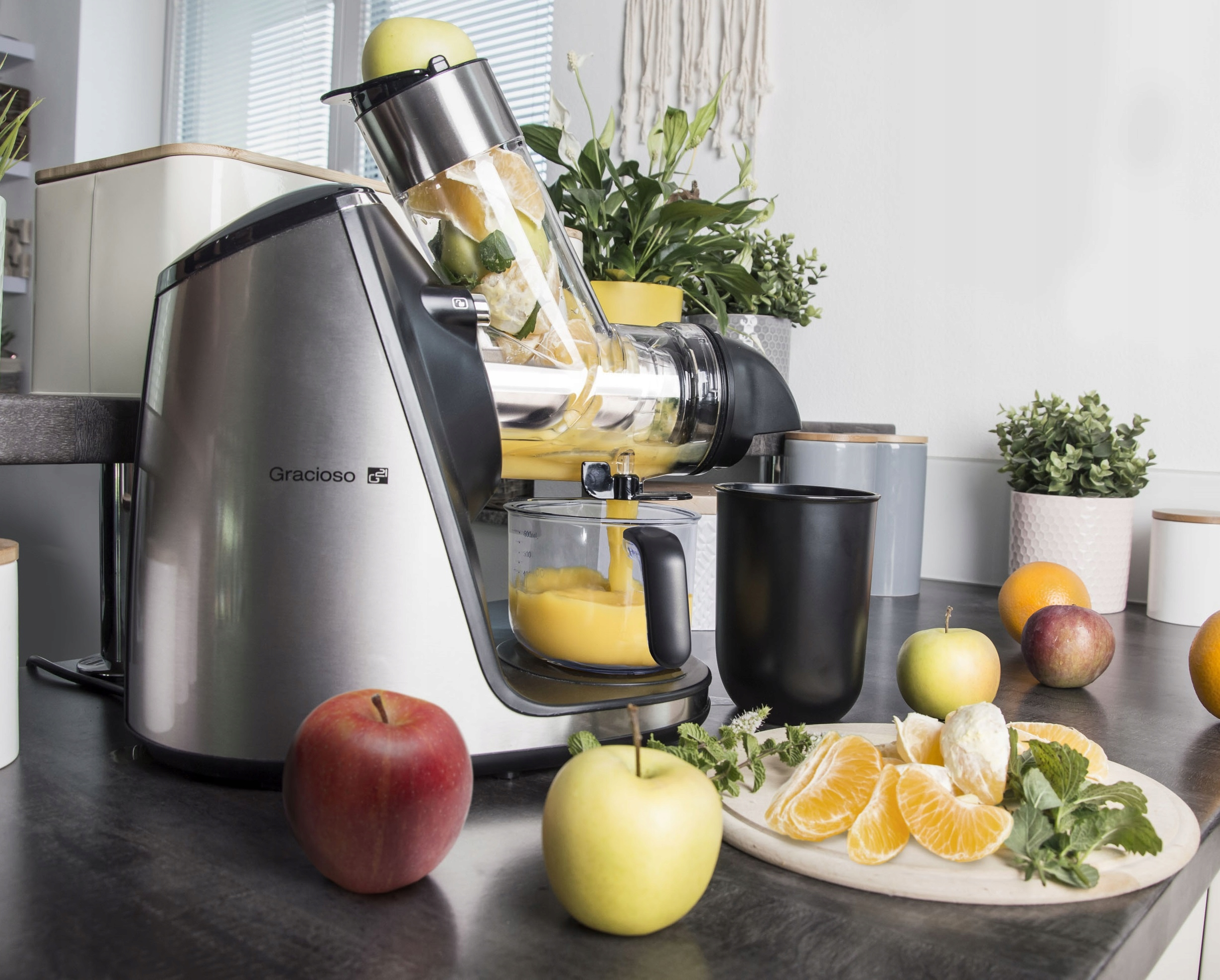 Wyiskarka z jabłkami i pomarańczami. Robiony jest sok. Pokrojone pomarańcze i jabłka leżą na drewnianej desce.