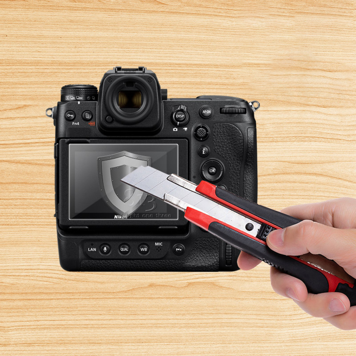 Ręka trzymająca nożyk ma zamiar przeciąć osłonę ekranu na czarnym aparacie. Tło to drewniana powierzchnia.