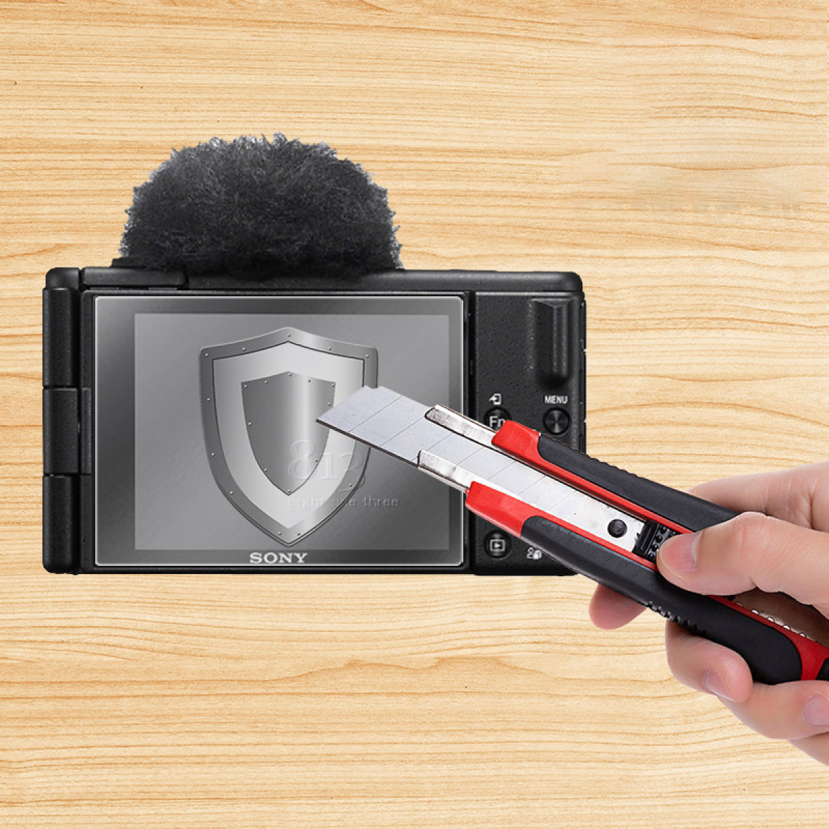 Osoba tnie ochraniacz ekranu na czarnym aparacie. Aparat znajduje się na drewnianej powierzchni.