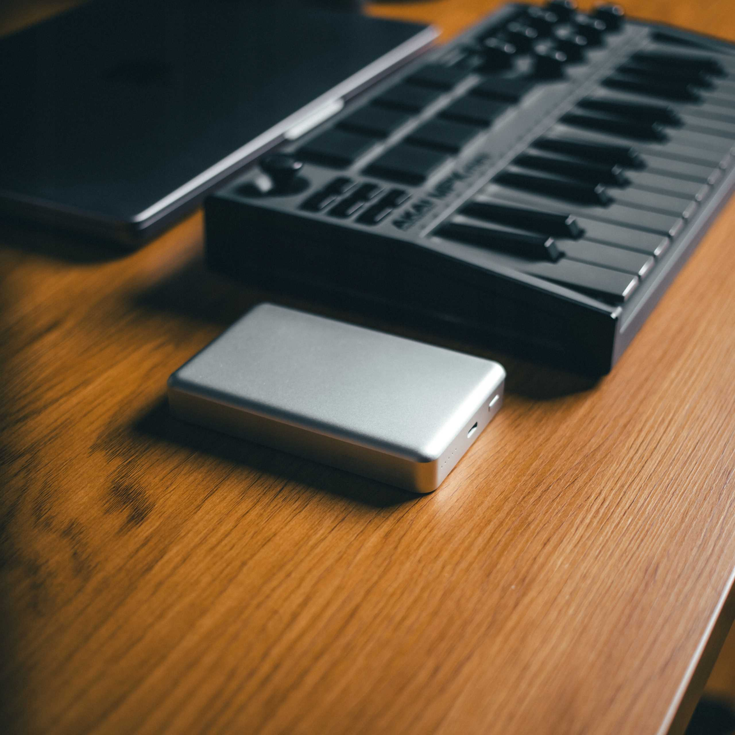 Drewniane biurko z laptopem, klawiaturą MIDI i srebrnym dyskiem zewnętrznym.