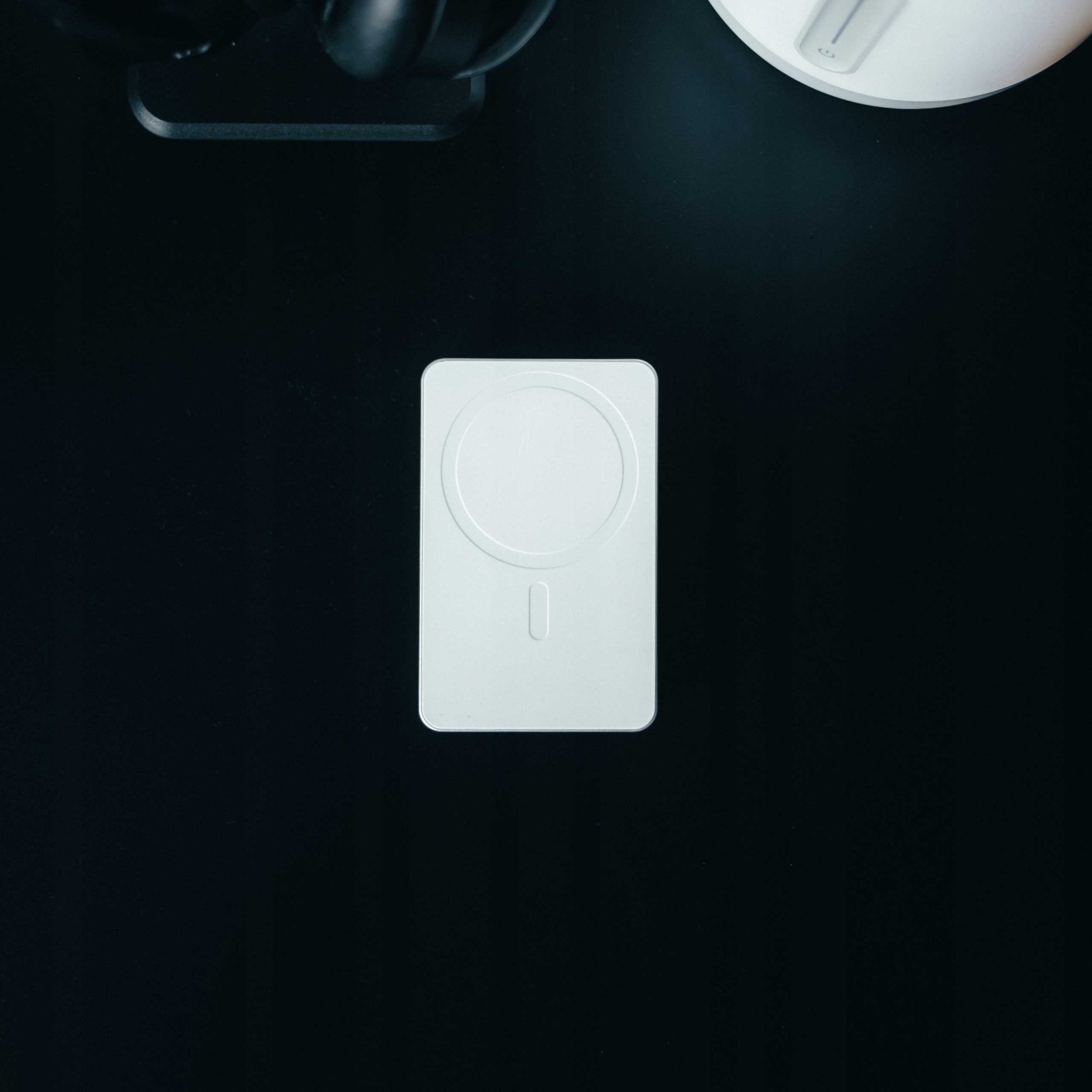 Biała ładowarka bezprzewodowa na czarnej powierzchni. Słuchawki i biały przedmiot widoczne.