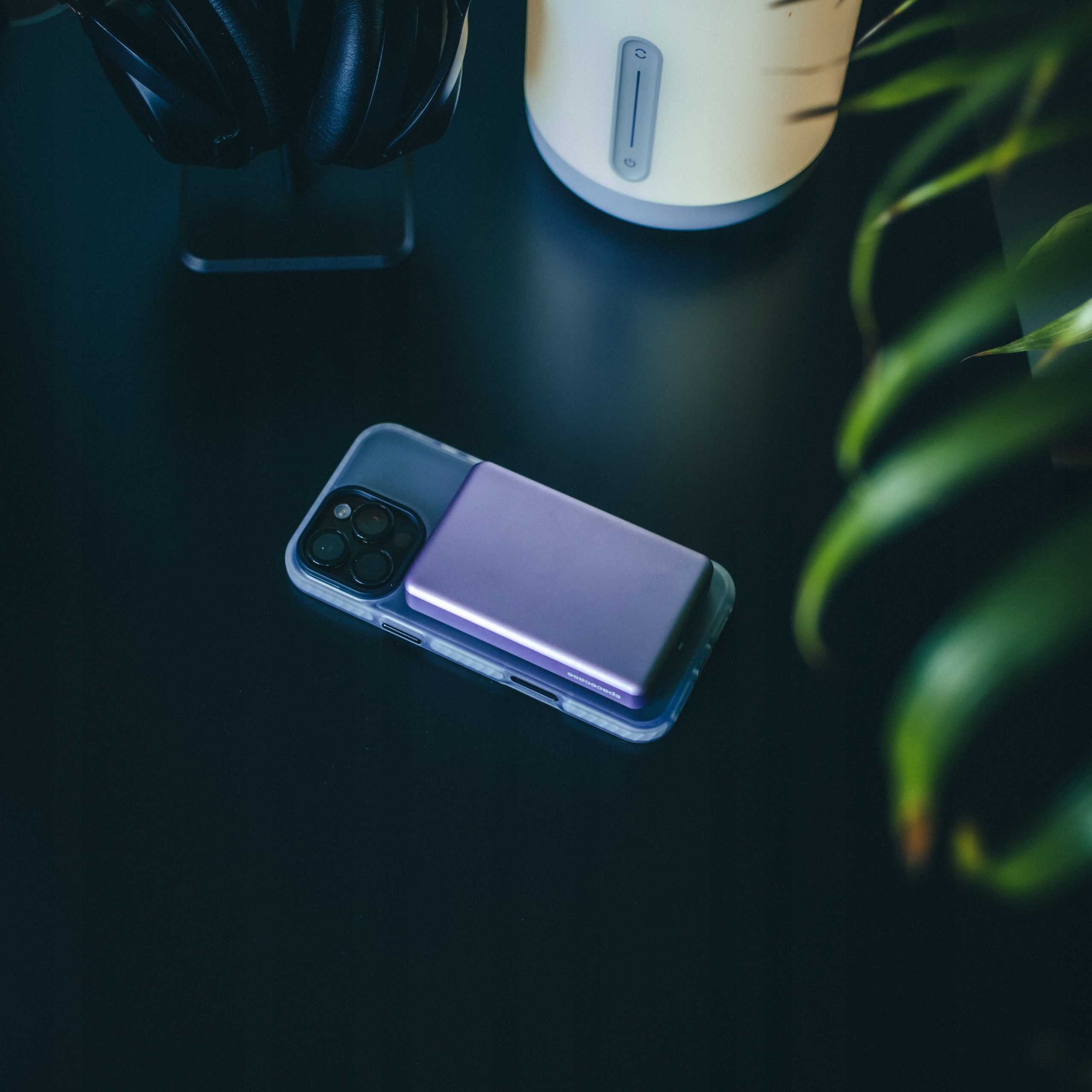 Telefon z fioletowym power bankiem na czarnej powierzchni. Widoczne są również słuchawki i białe urządzenie.