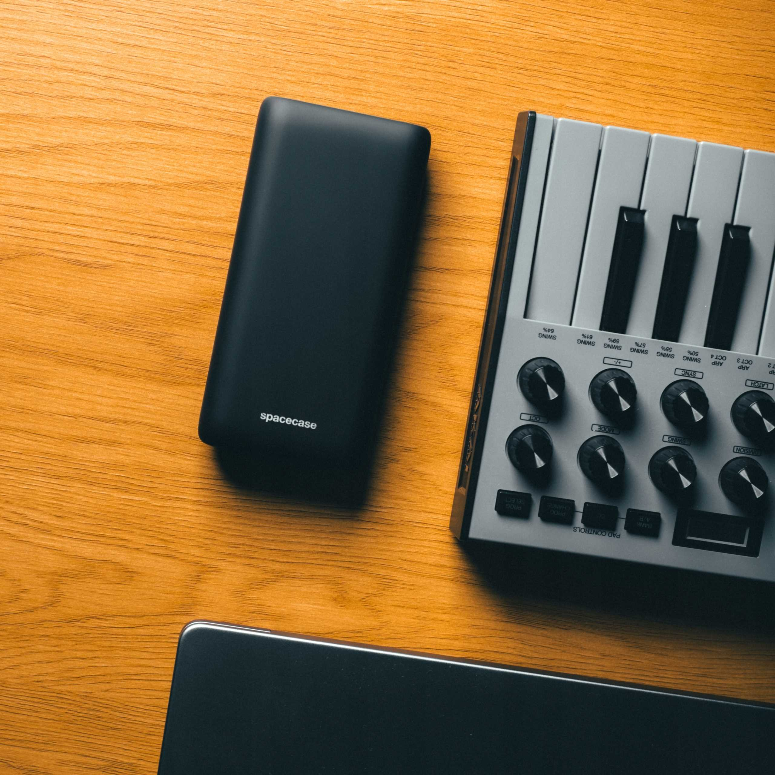 Czarny power bank i szary syntezator na drewnianej powierzchni. Power bank ma napis spacecase.