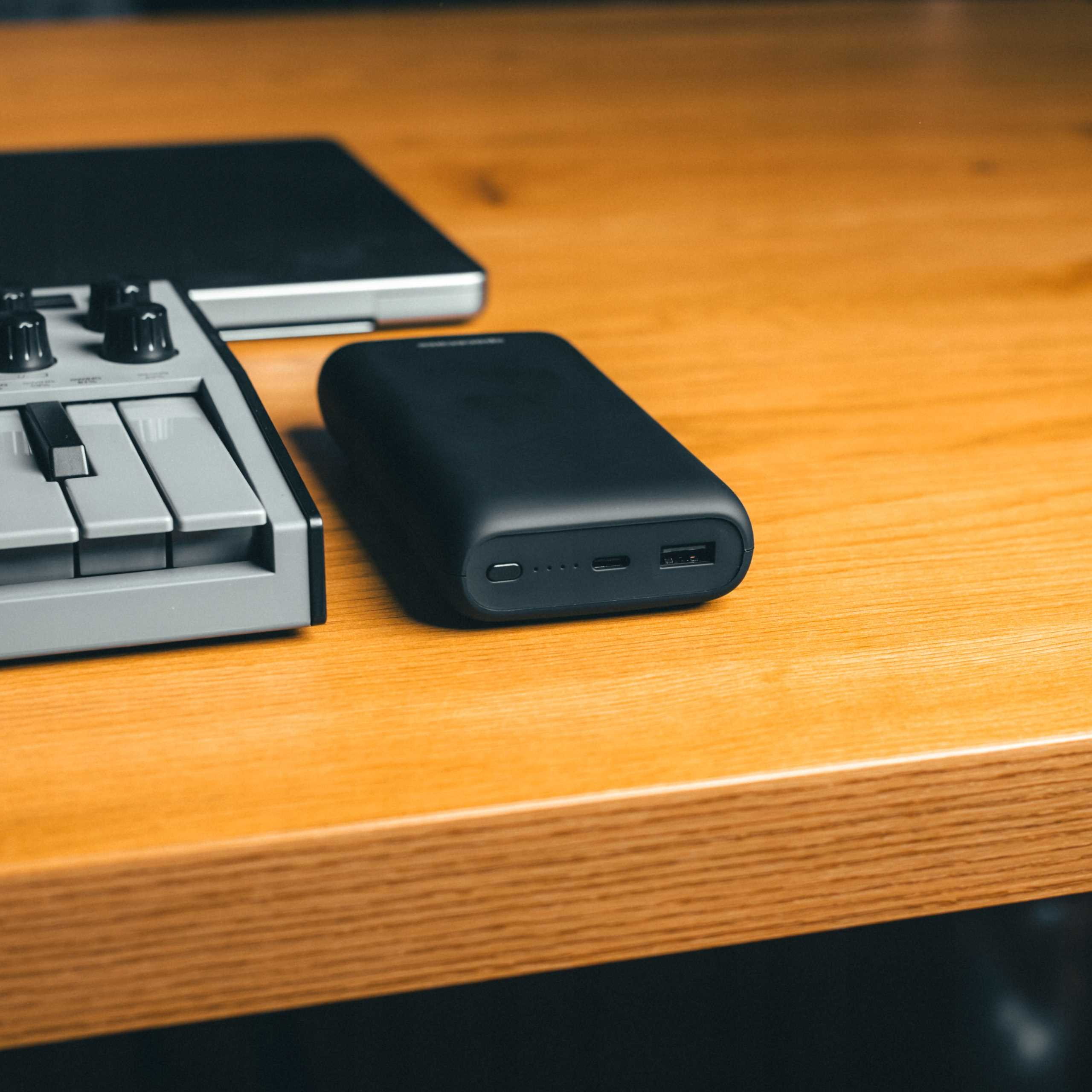 Czarny power bank, mini klawiatura i laptop na drewnianej powierzchni.