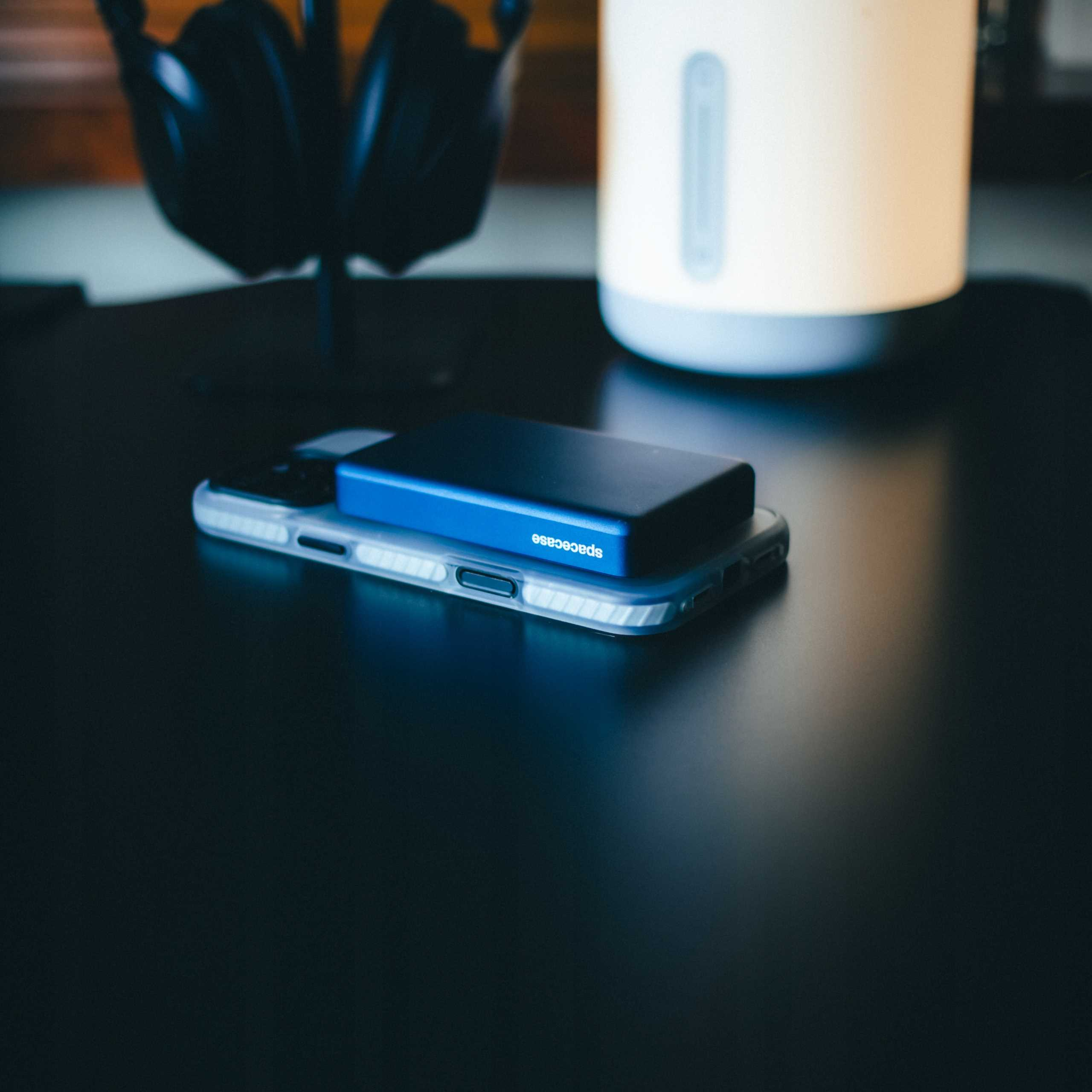 Telefon z niebieskim urządzeniem na górze, umieszczony na czarnej powierzchni. Słuchawki i biała lampa w tle.