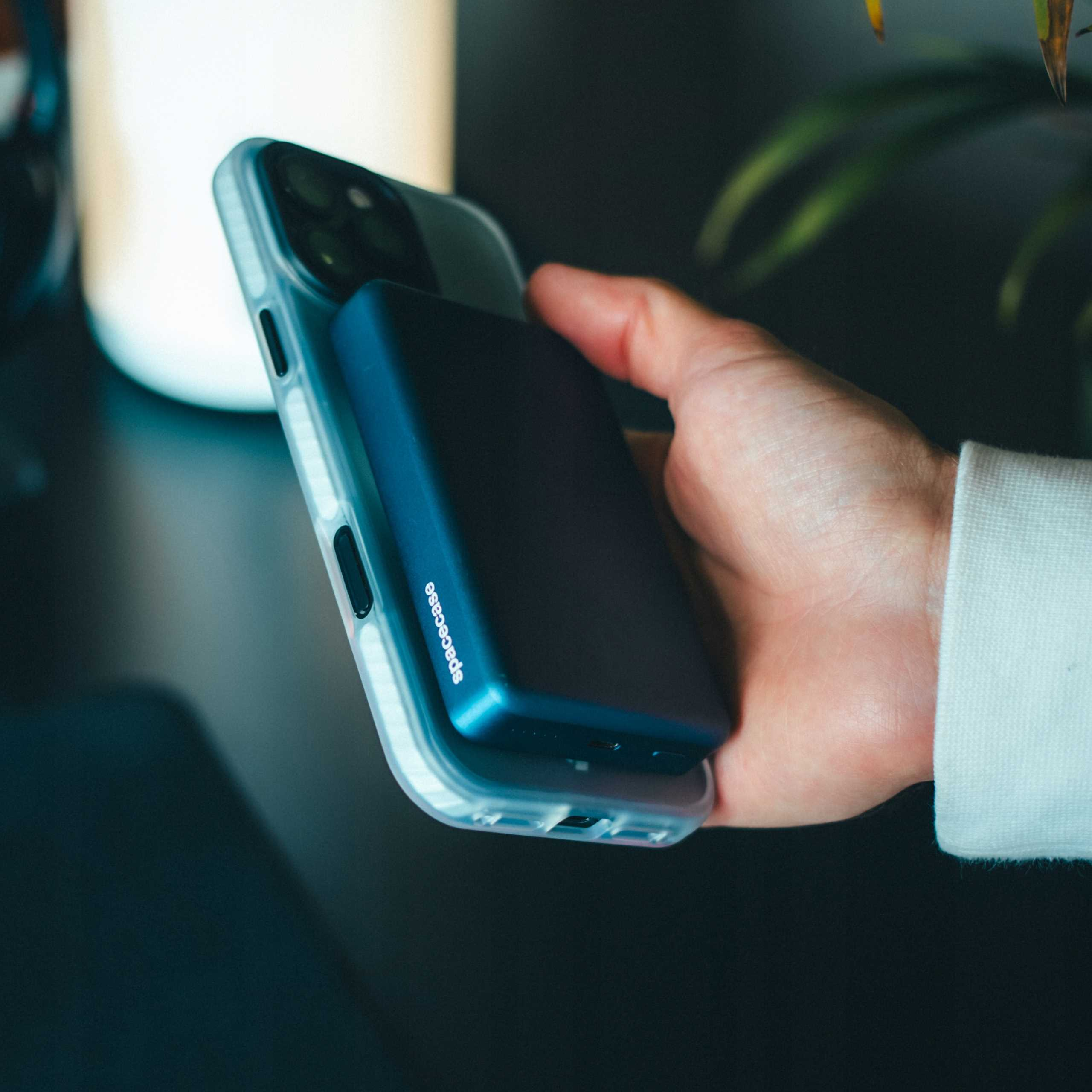 Ręka trzyma telefon w przezroczystym etui z niebieskim power bankiem. Power bank ma napis 'spacecase'.
