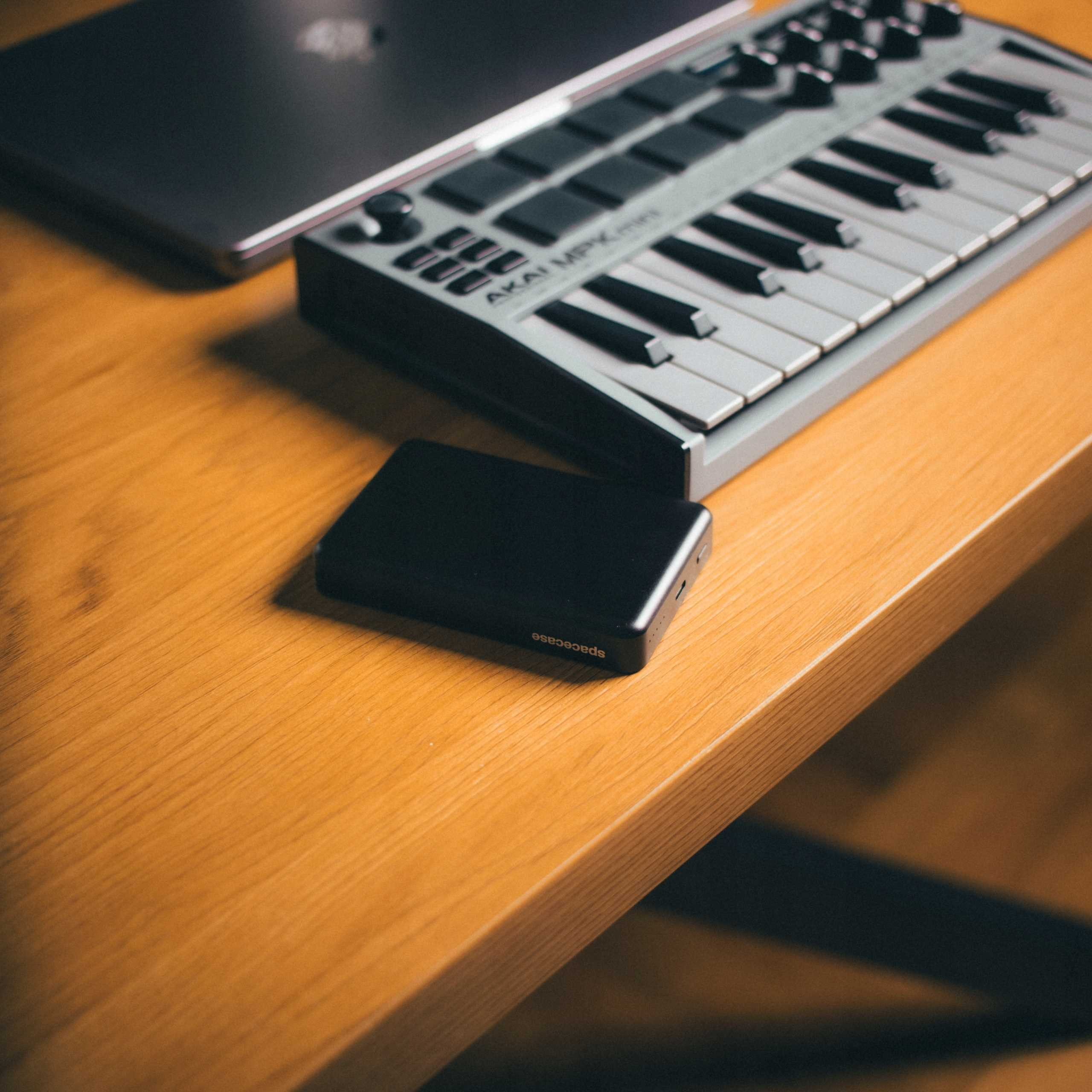 Biurko z laptopem, klawiaturą MIDI i czarnym zewnętrznym dyskiem twardym. Biurko jest drewniane.