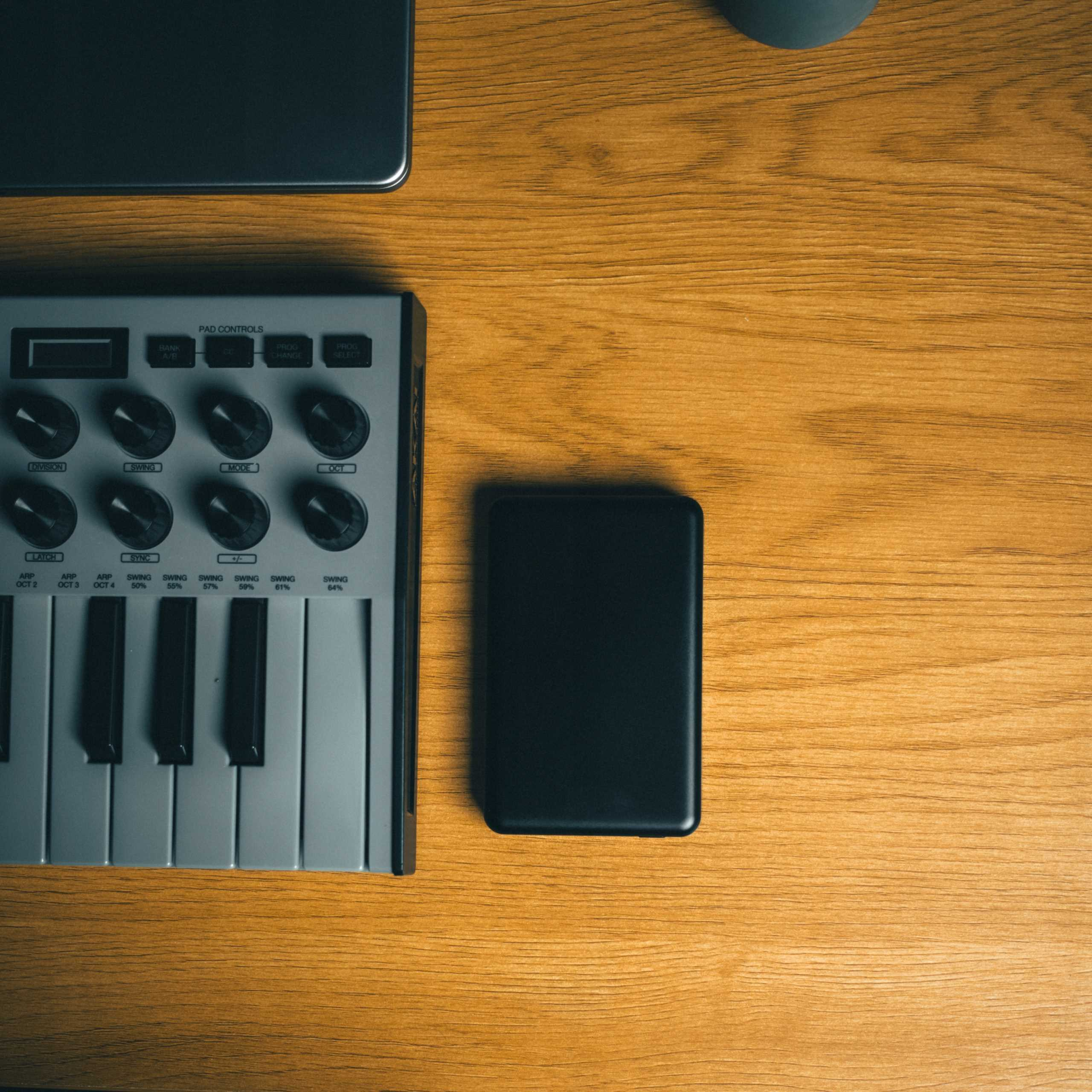 Drewniane biurko z klawiaturą, czarnym urządzeniem i ciemnoszarym laptopem. Widok z góry, zdjęcie studyjne.