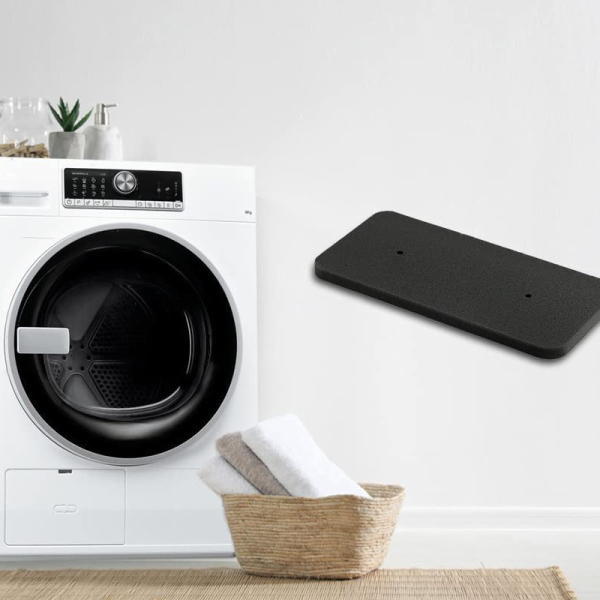 Pralka stoi obok plecionego kosza z ręcznikami. Czarna prostokątna deska znajduje się w tle.