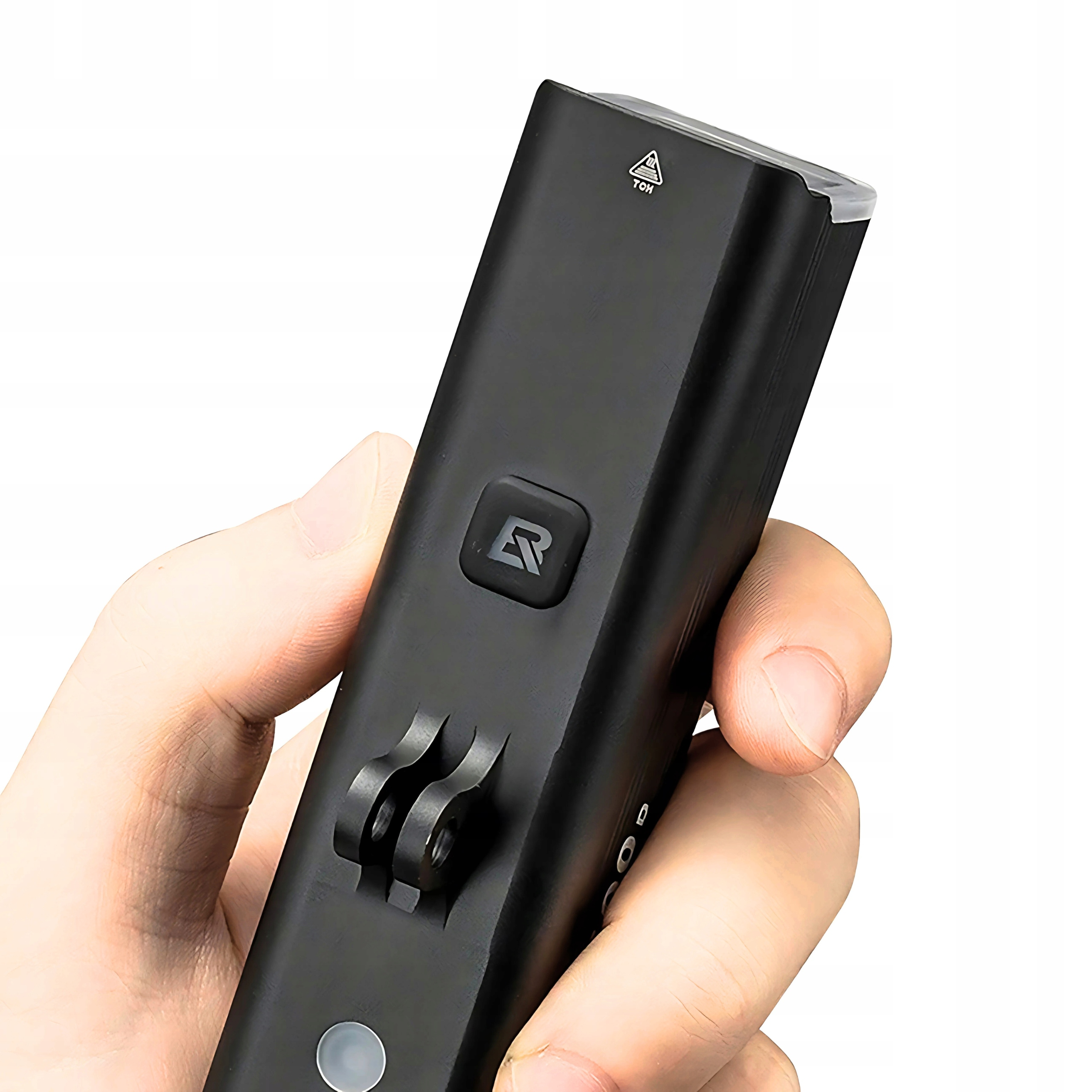 Czarna lampa rowerowa trzymana w dłoni. Lampa ma uchwyt i przycisk. Białe tło.