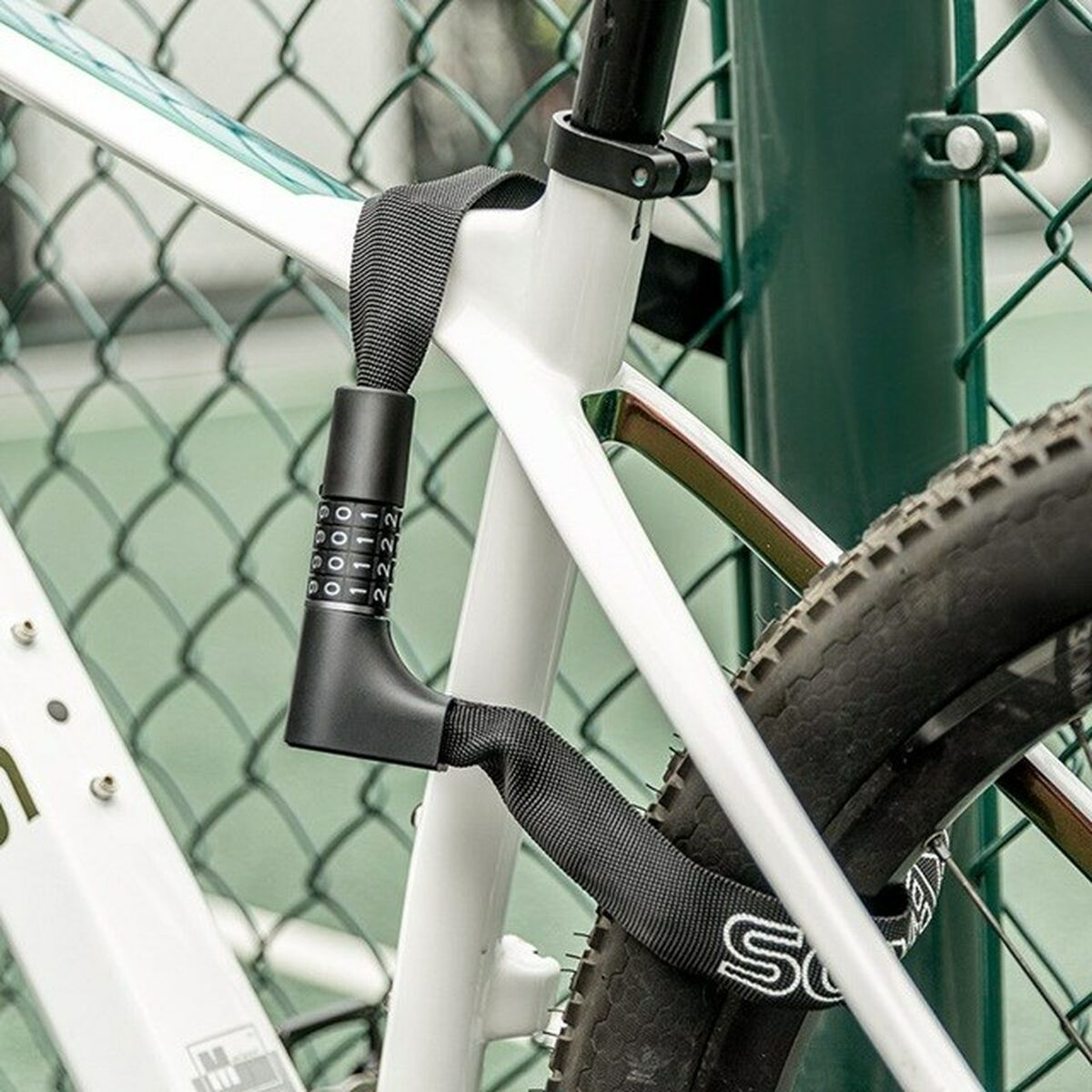 Biały rower jest zablokowany czarną blokadą szyfrową. Zamek jest wokół ramy i opony, w pobliżu zielonego ogrodzenia.