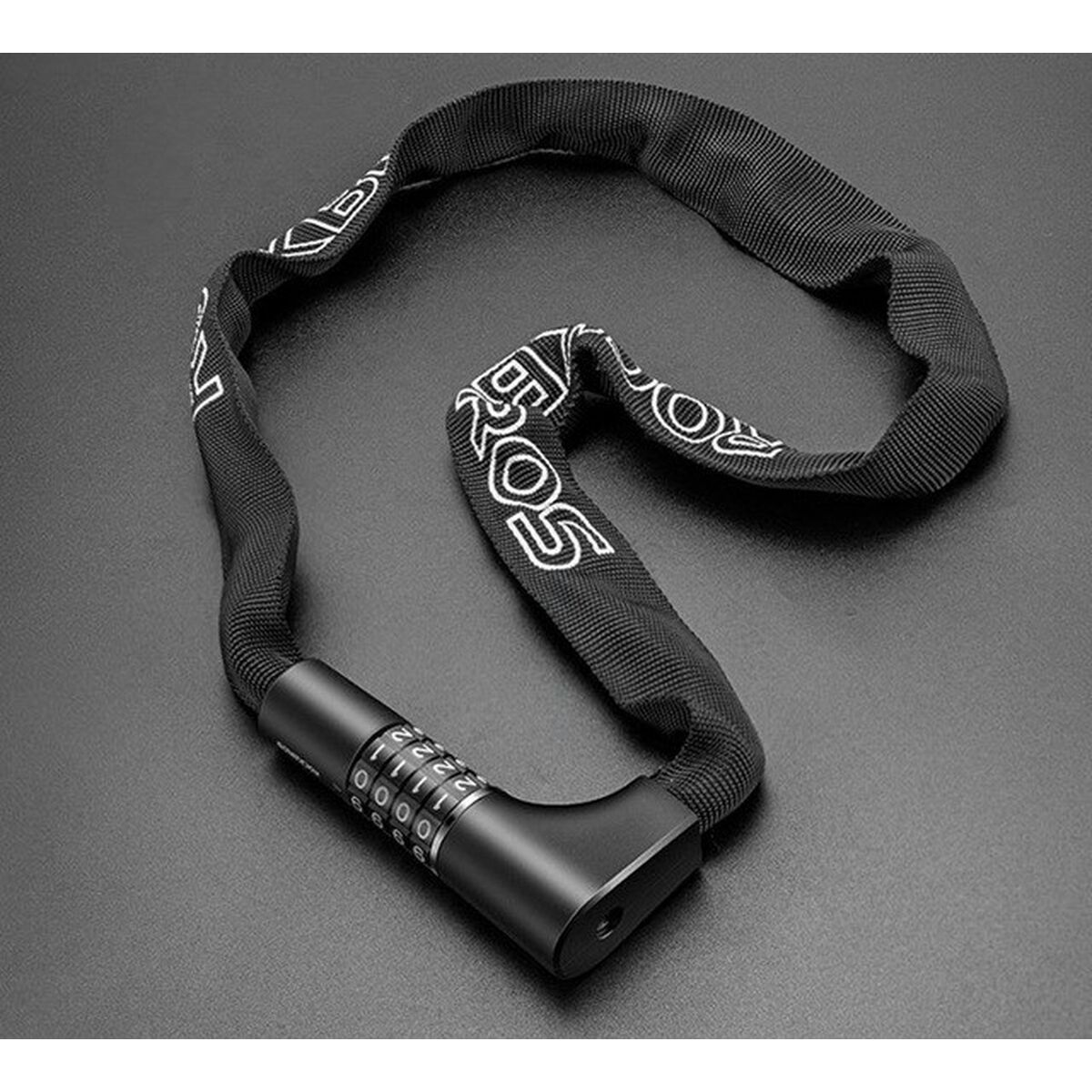 Czarna blokada łańcucha rowerowego z zamkiem szyfrowym. Zamek jest na szarej powierzchni. Łańcuch ma biały tekst.