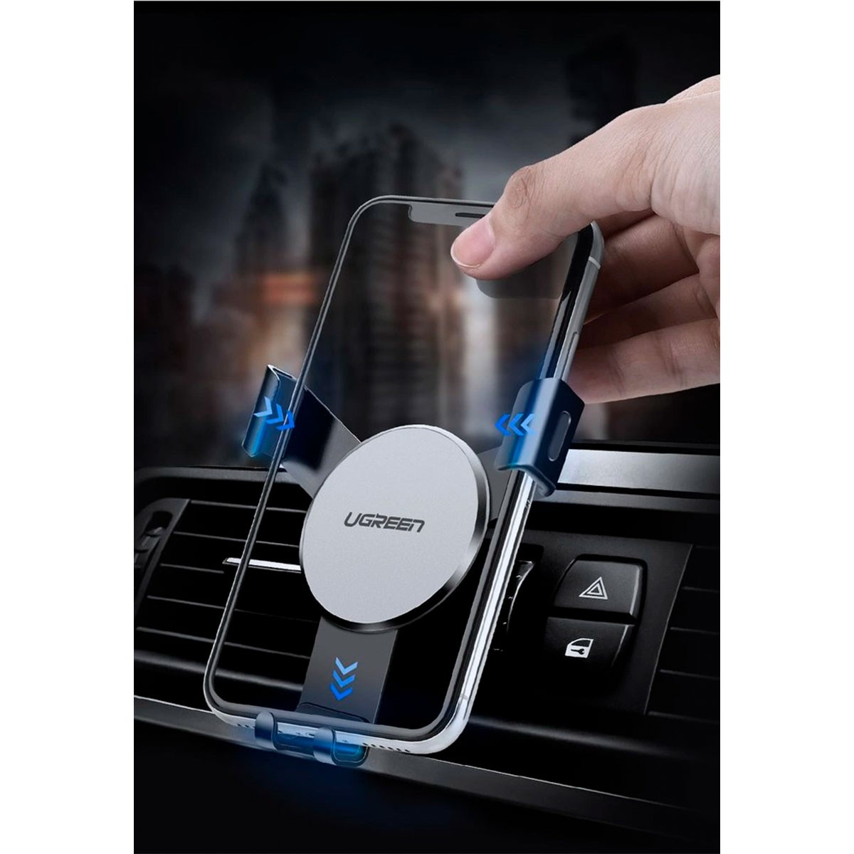Dłoń trzymająca telefon nad uchwytem wentylacyjnym samochodu. Uchwyt ma srebrne logo UGREEN. Widoczne przyciski awaryjne i blokady samochodu.