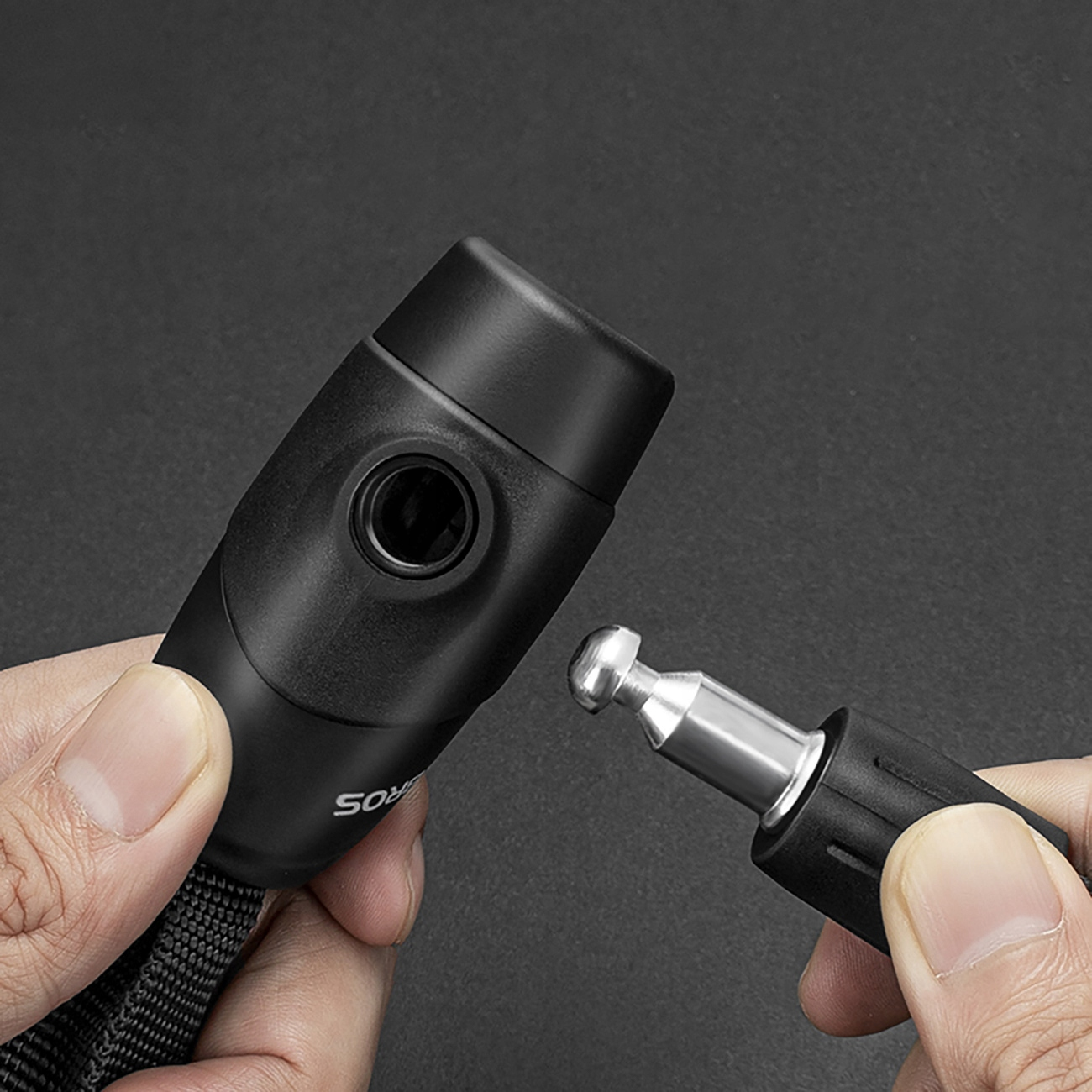 Dłonie trzymają czarną kłódkę ze srebrnym metalowym elementem. Tło jest ciemnoszare.