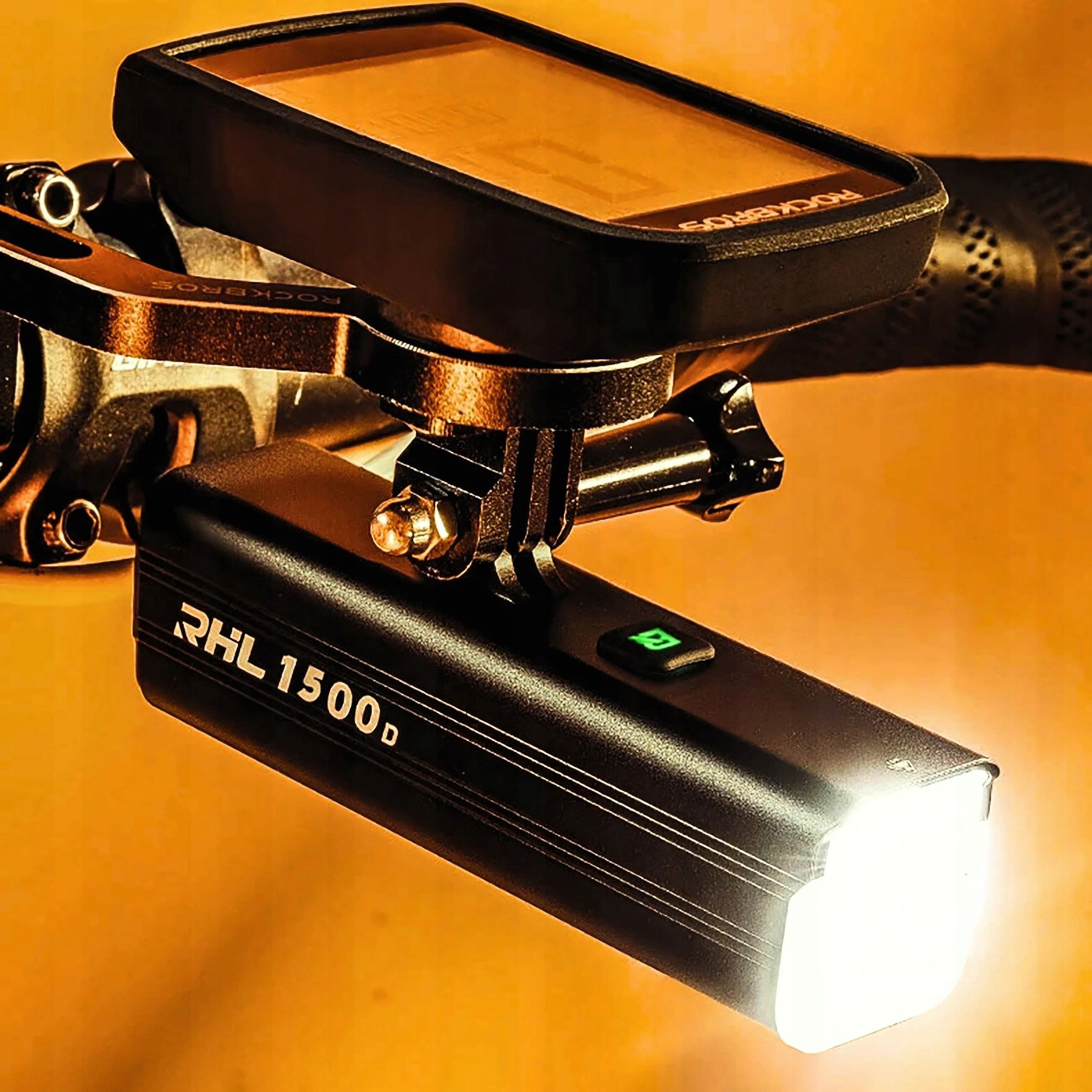 Światło rowerowe i komputer rowerowy są zamontowane na kierownicy. Światło jest włączone. Tło jest pomarańczowe.