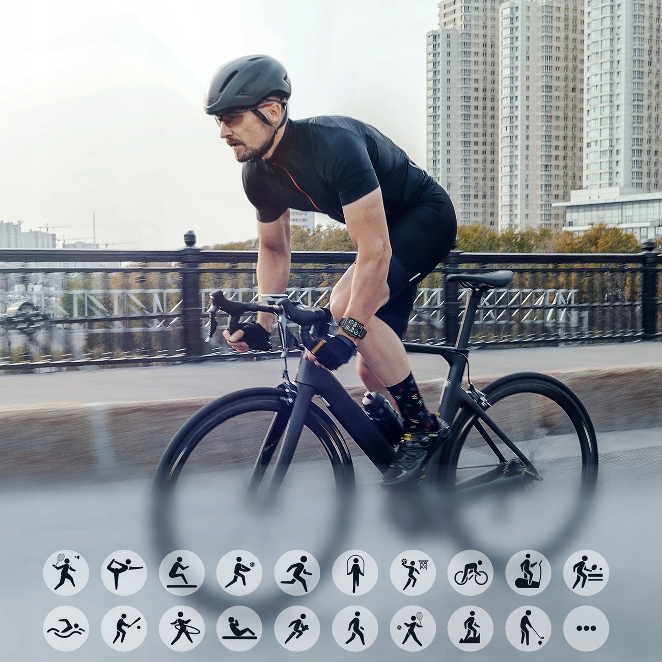 Kolarz na czarnym rowerze na moście. Ma kask i czarne ubrania. Budynki w tle.