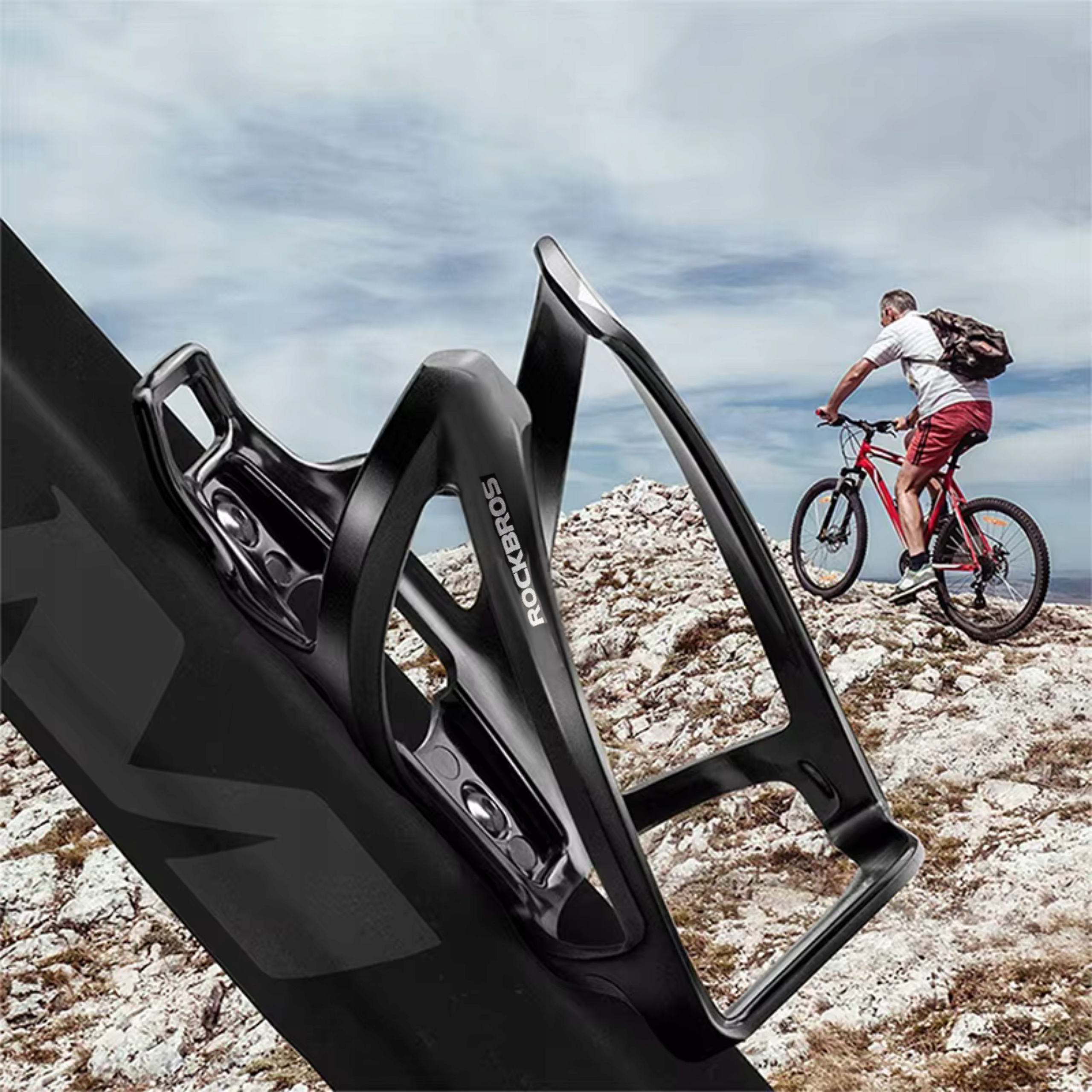 Czarny uchwyt na butelkę rowerową jest na ramie roweru. Kolarz jedzie po skalistym terenie.