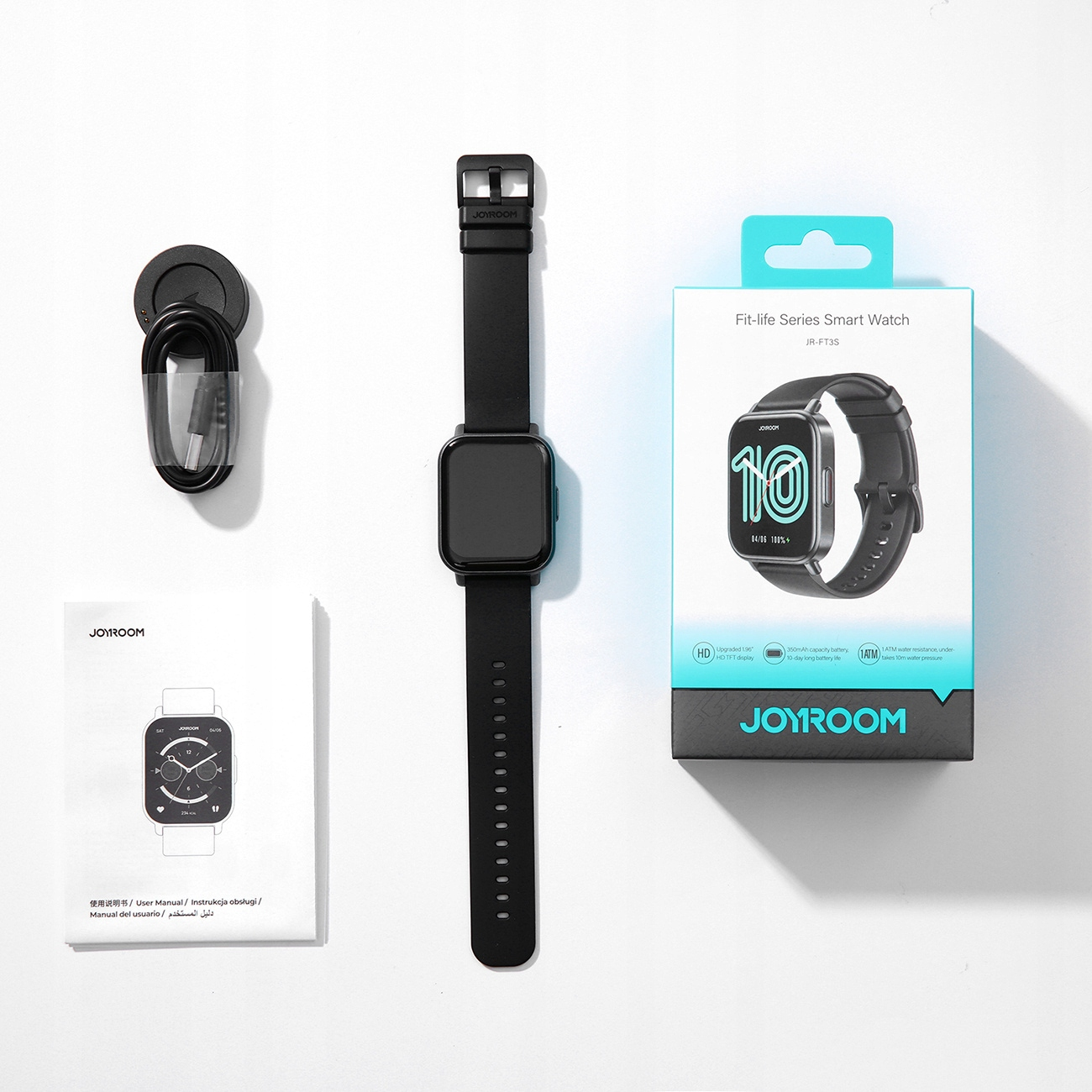 Czarny smartwatch z pudełkiem, ładowarką i instrukcją na białej powierzchni. Zegarek pokazuje liczbę 10 na ekranie.