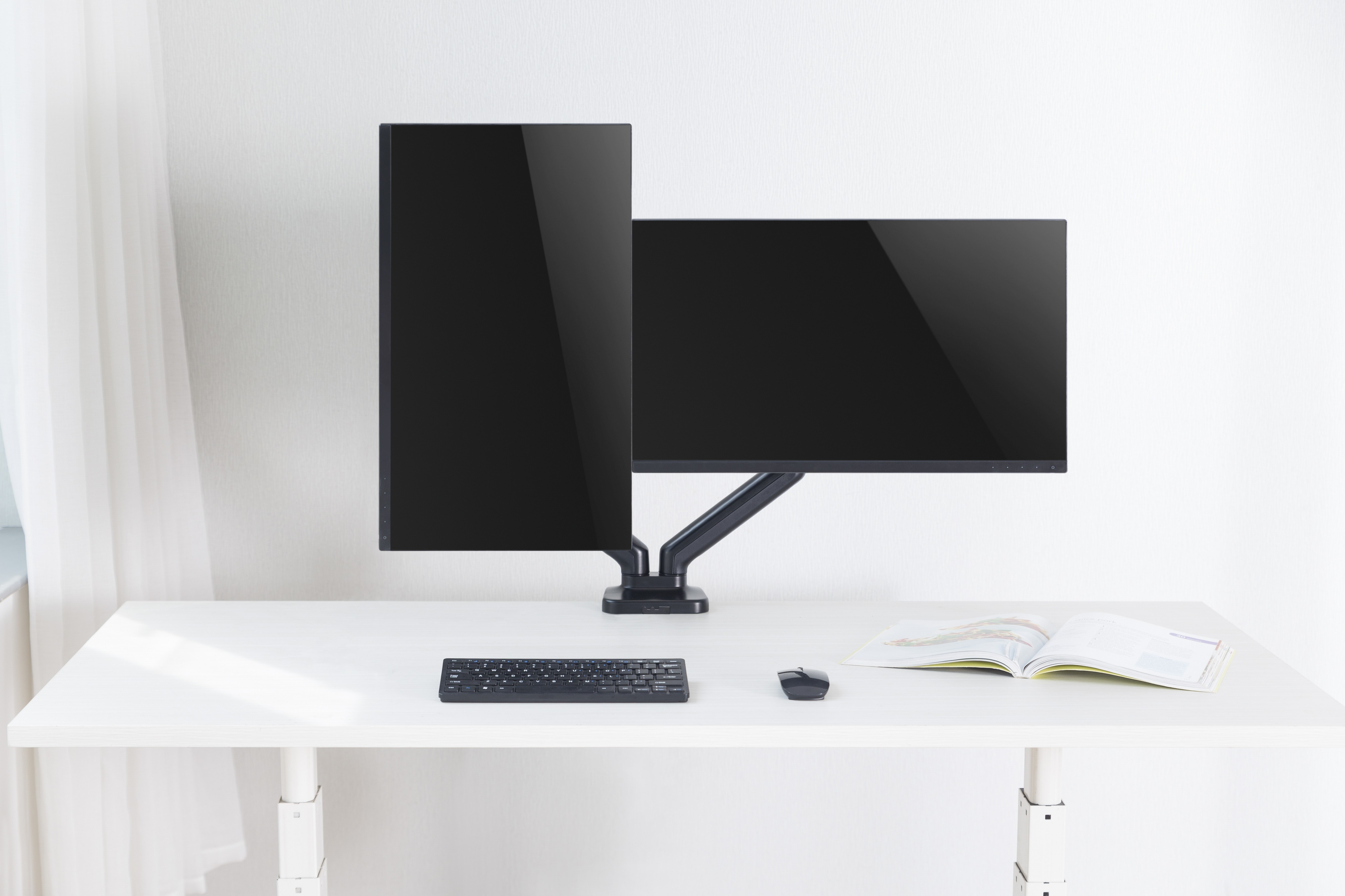 A modern desk setup with two black monitors, keyboard, mouse, and an open book on a white desk.