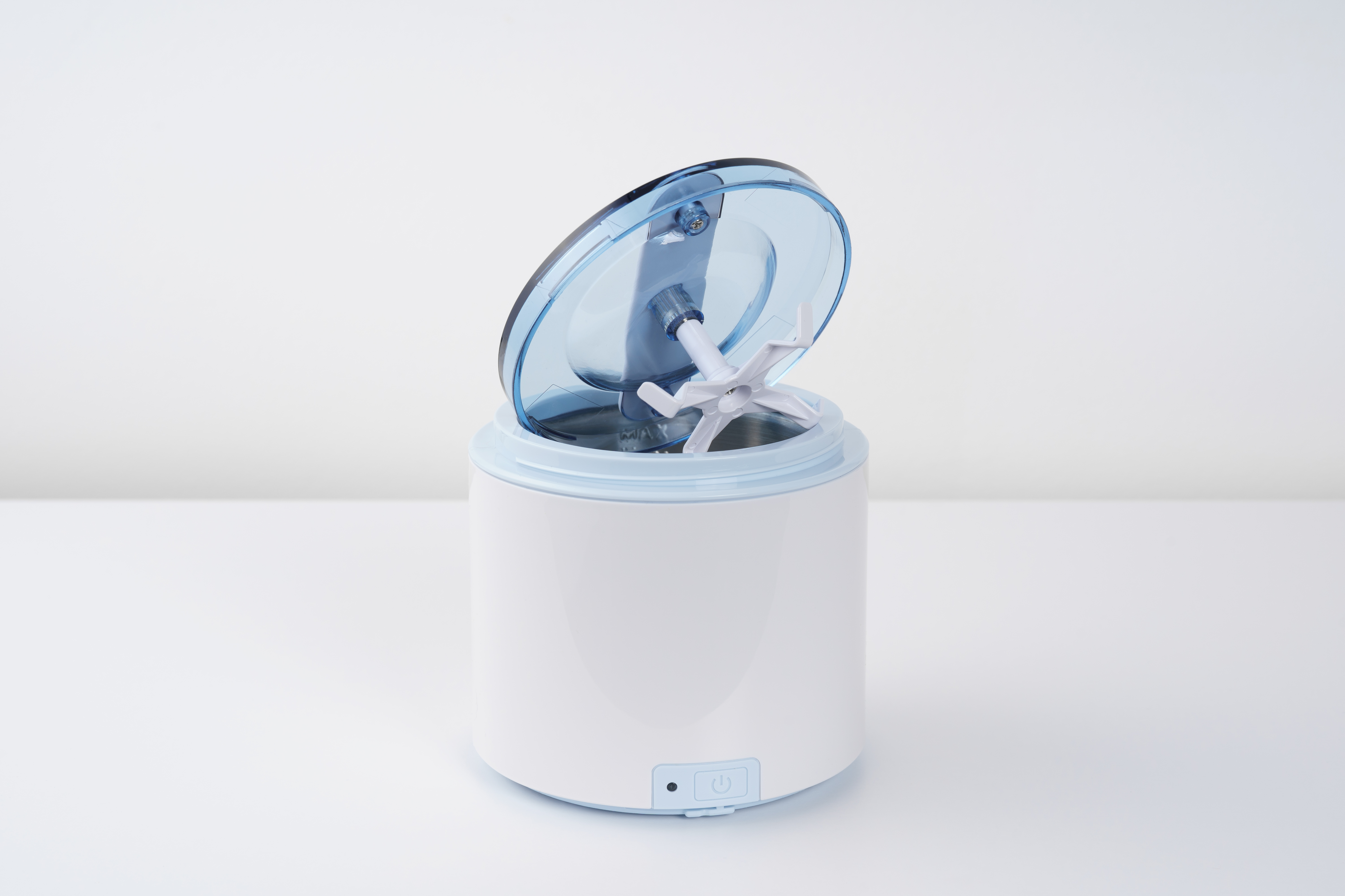 Biało-niebieska maszyna do lodów. Pokrywa jest otwarta, widać białe ostrze mieszające. Na białej powierzchni.