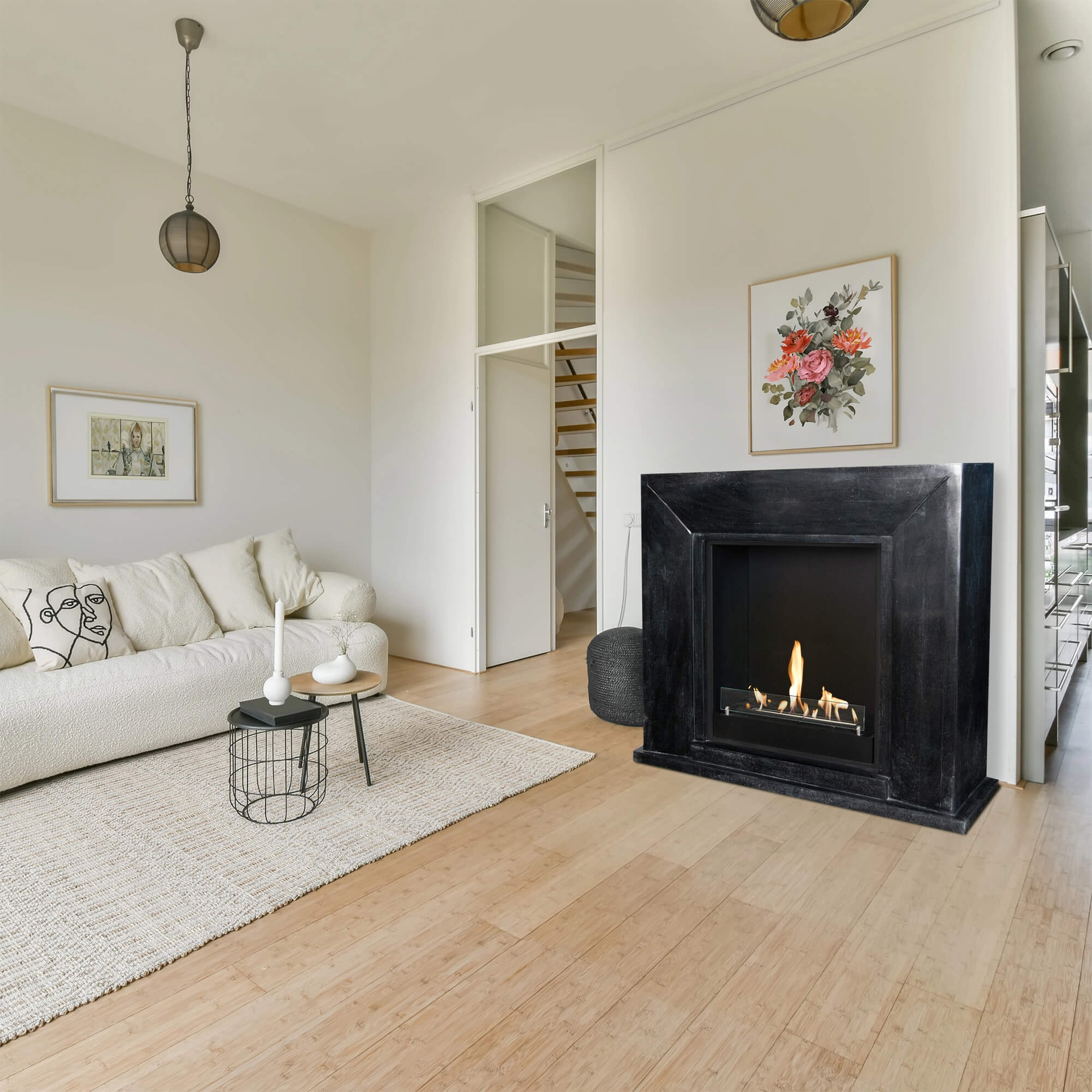 Living room with white sofa, fireplace, floral art. Wooden floor and rug. Light fixtures and door to stairs.