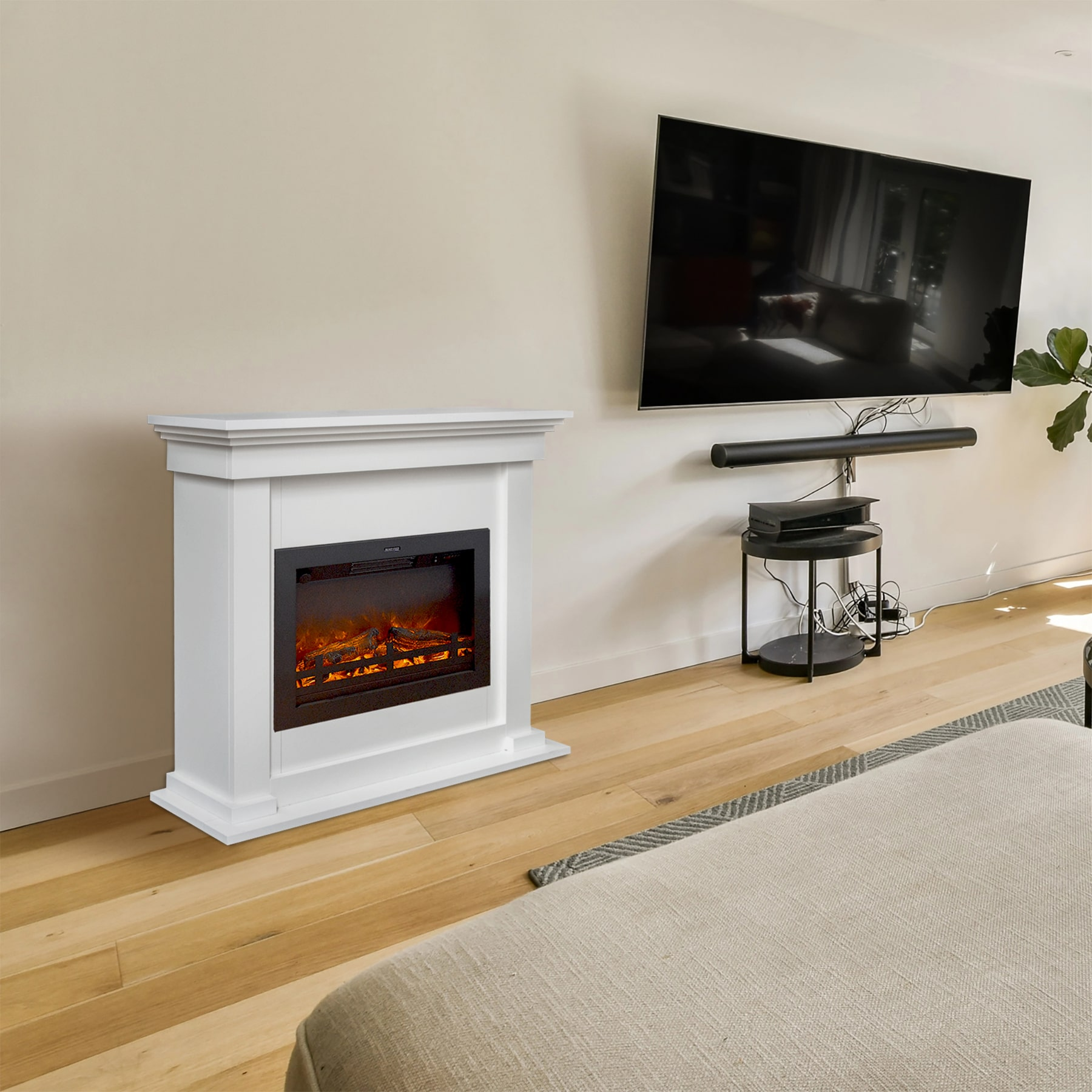 Een witte elektrische open haard met een gloeiend vuureffect, een tv en een kleine zwarte tafel in een kamer met houten vloeren.