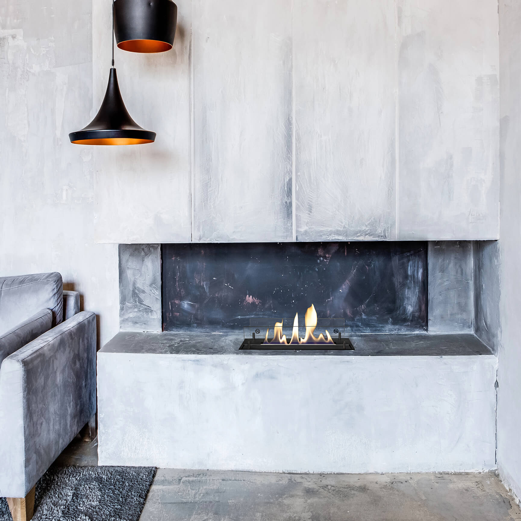 Moderne woonkamer met open haard. Zwarte lampen hangen erboven. Vlammen branden in de open haard. Grijze bank links.