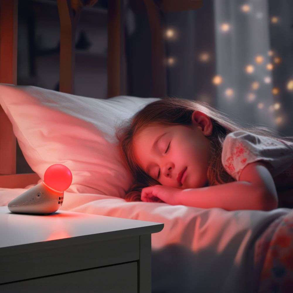 Ein junges Mädchen schläft friedlich im Bett. Ein Nachtlicht mit rotem Schein steht auf einem Nachttisch. Die Szene ist sanft beleuchtet.