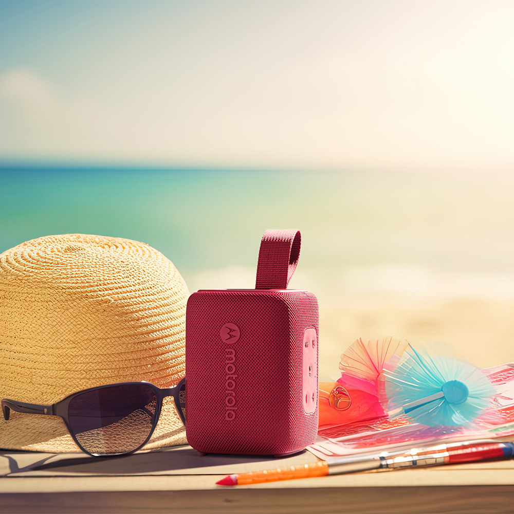 Un altoparlante Motorola rosso, occhiali da sole, cappello di paglia, scena sulla spiaggia con mare e cielo, ombrellini da cocktail e penna su tavolo di legno.